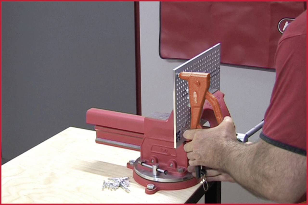 A person pulls a bending lever to bend a sheet metal using an angular clamping device. Screws are lying in the foreground.