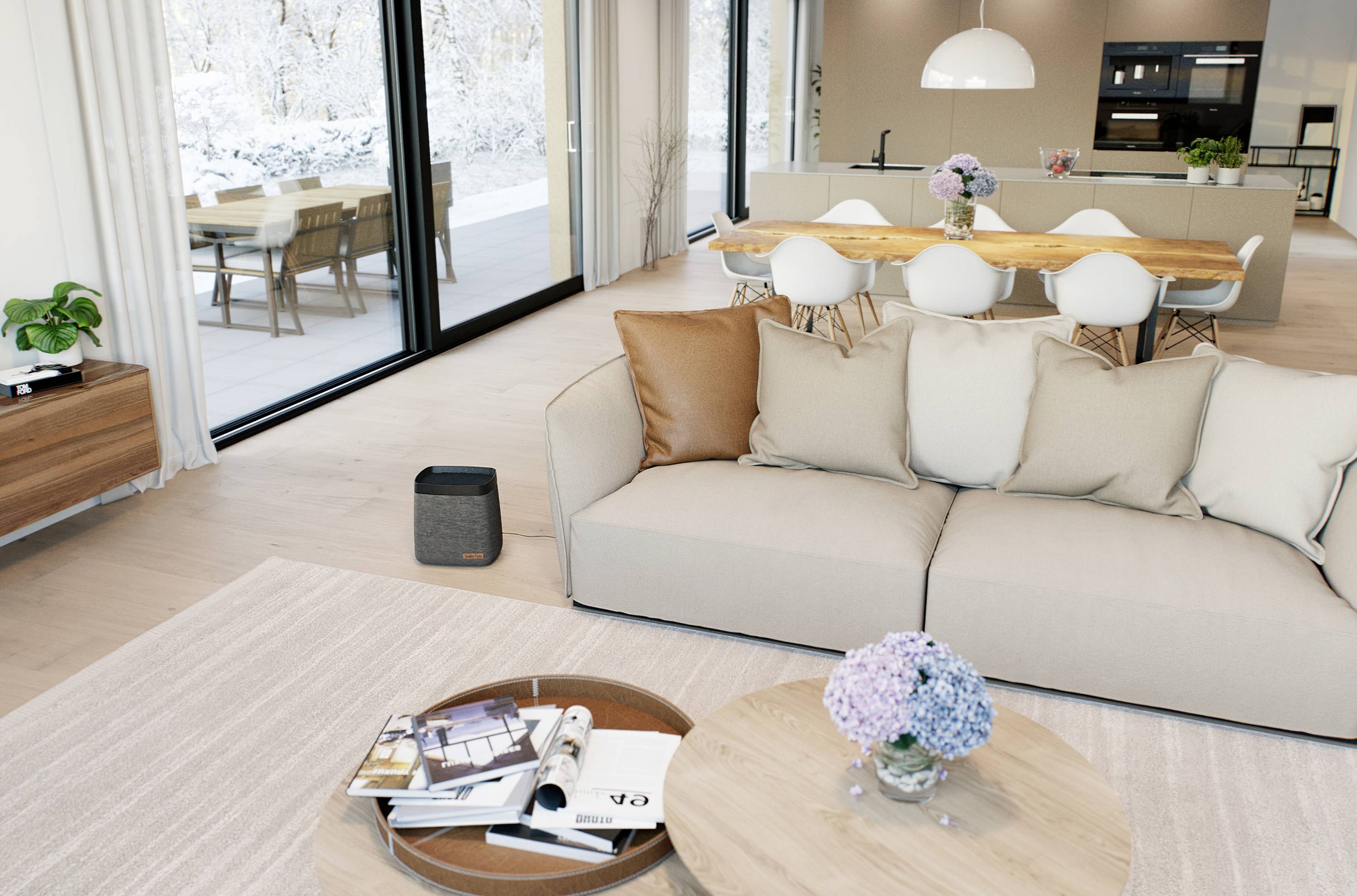Open-plan living room with a beige sofa, coffee table with flowers, dining area in the background. Large windows reveal a wintry terrace outside.