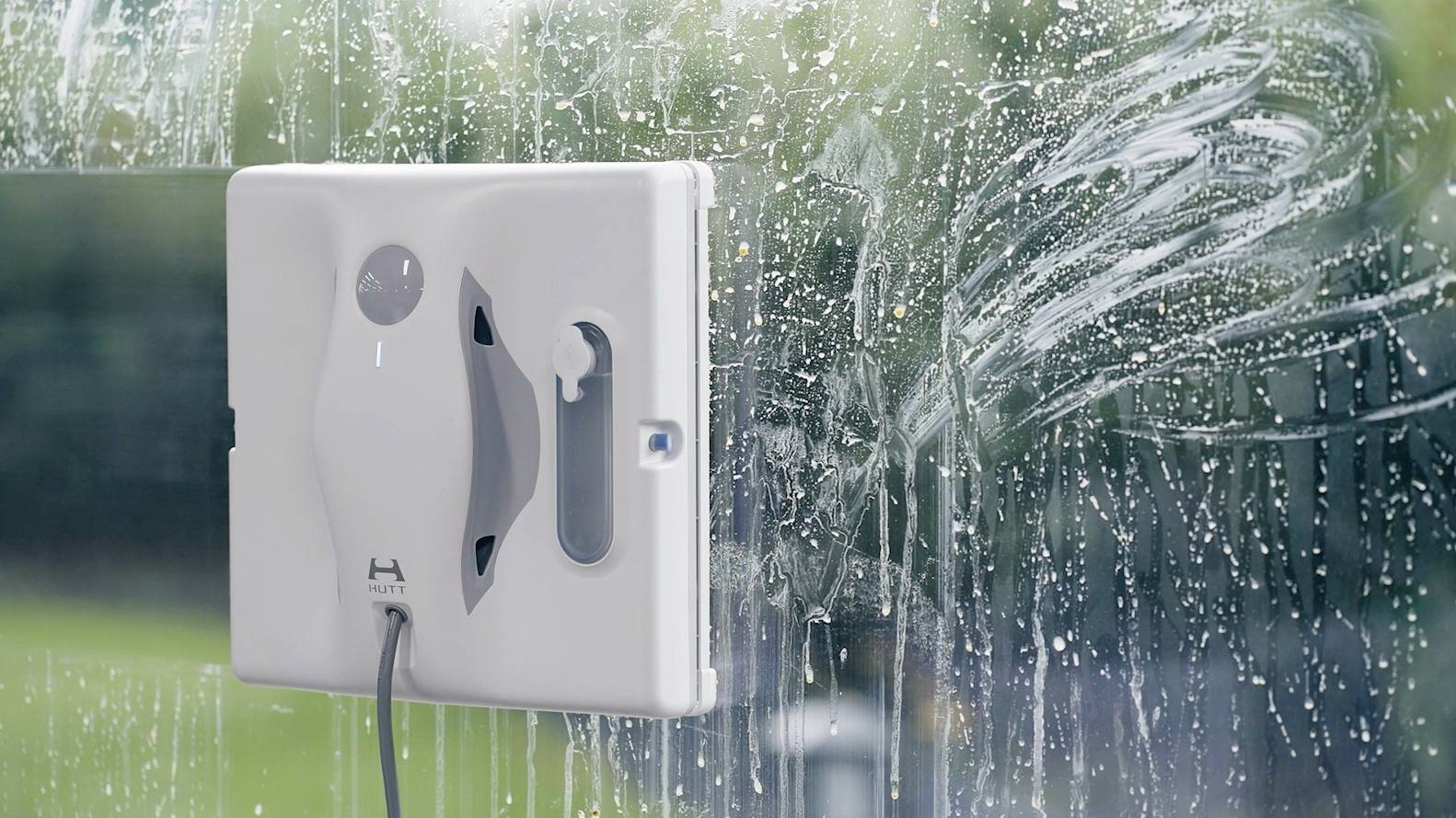 An automatic window cleaning robot is cleaning a glass window. Soapy water is visible as the robot glides across the surface.