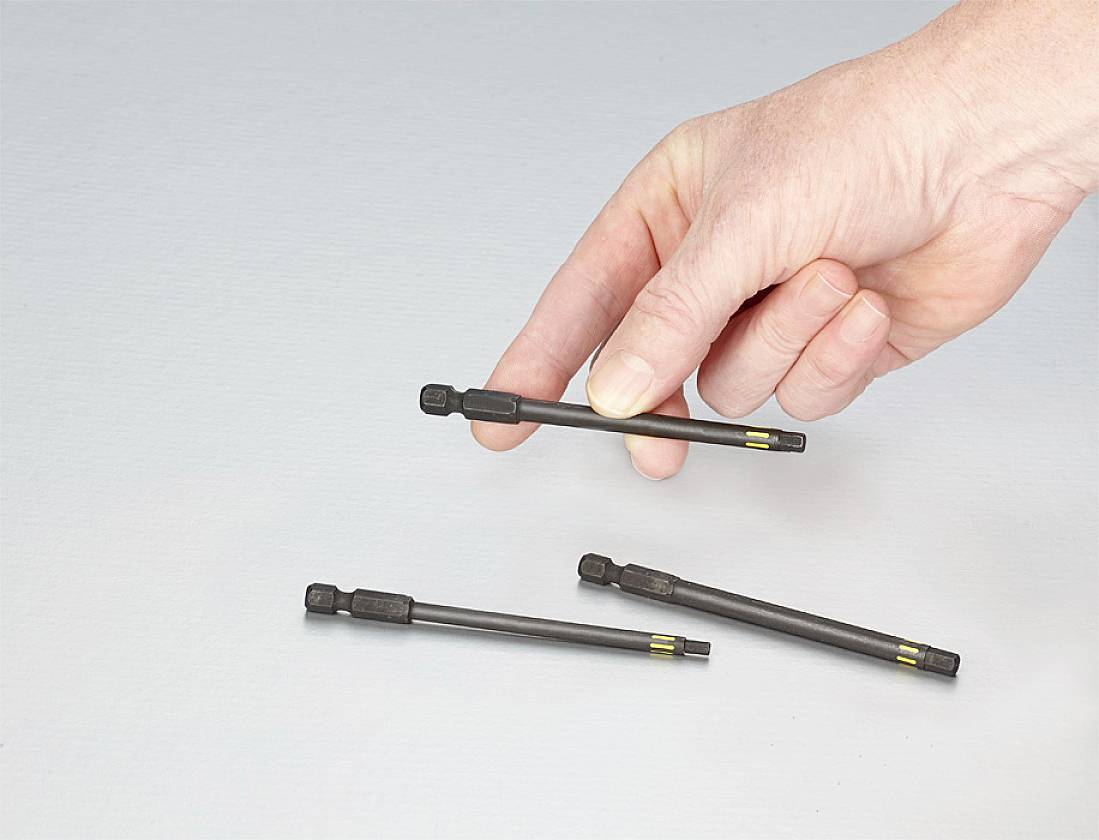 A hand is holding a magnetic screwdriver bit holder, with two additional ones lying on a grey surface.