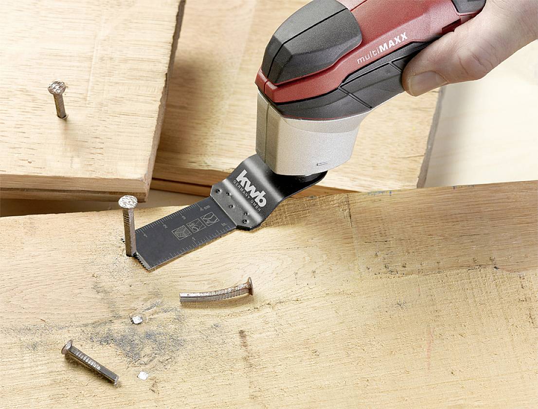 A person is using an oscillating multi-tool to cut a nail in a wooden board.