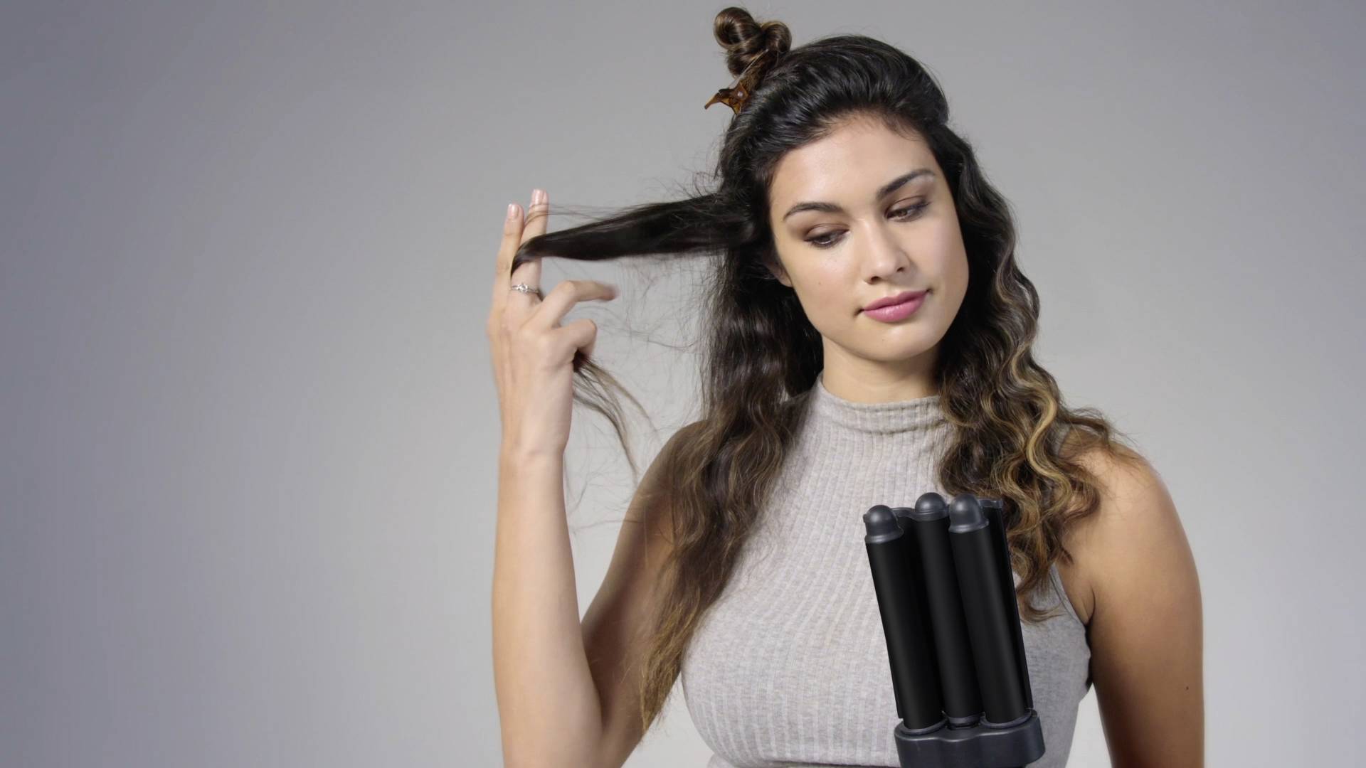A woman with long hair is using a hair styling device with multiple round cylinders. She is holding a strand of hair to style it.