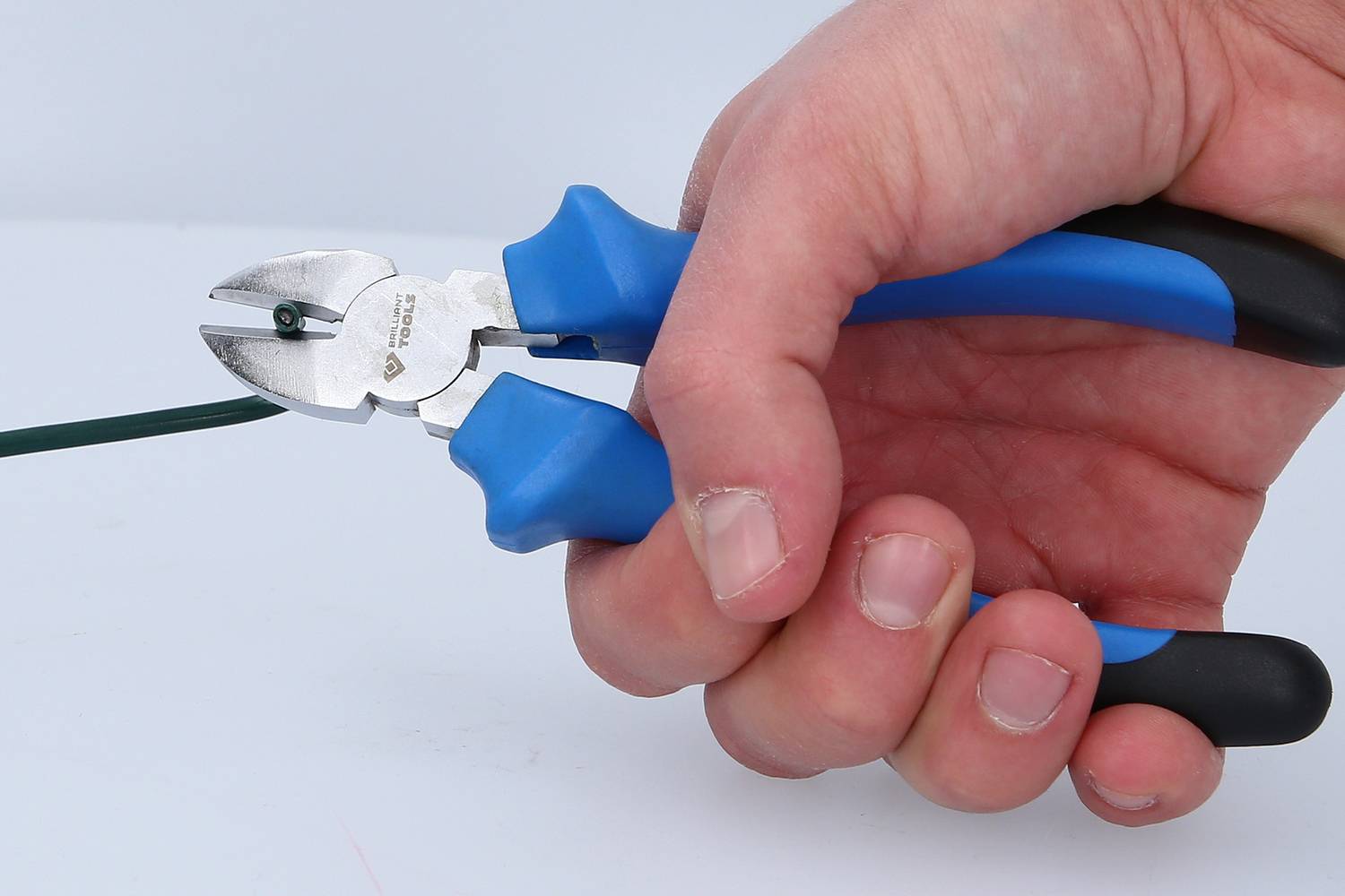 A hand is holding a pair of blue side cutters and cutting a green wire.