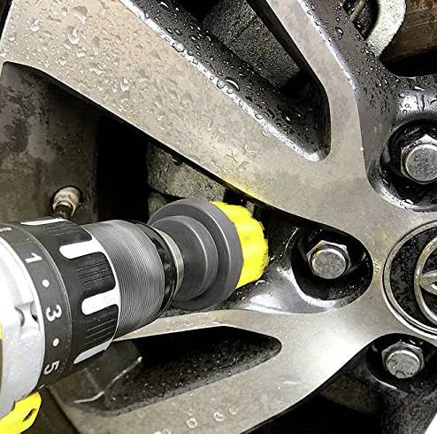 Drill with a yellow brush attachment cleaning a wet car tyre wheel. Close-up reveals water droplets and wheel bolt fixings.