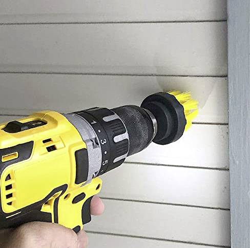 A yellow power drill with a brush attachment is cleaning a white wall panelling.