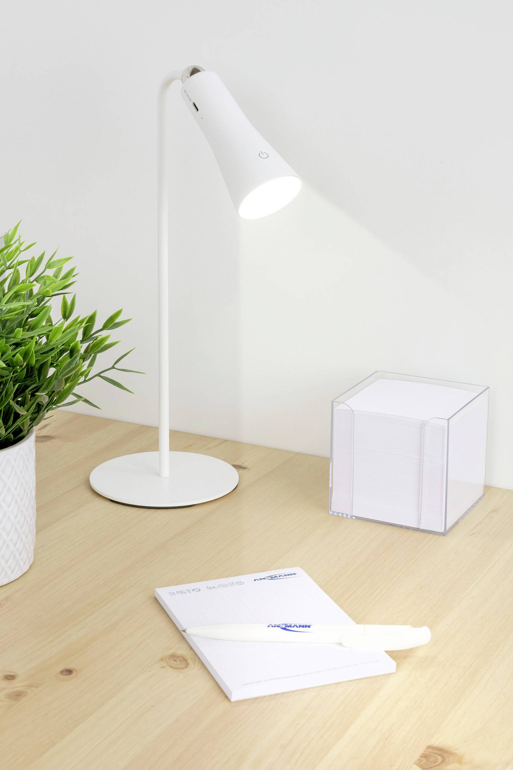 A minimalist desk with a switched-on white lamp, a notepad, a pen and a potted plant.