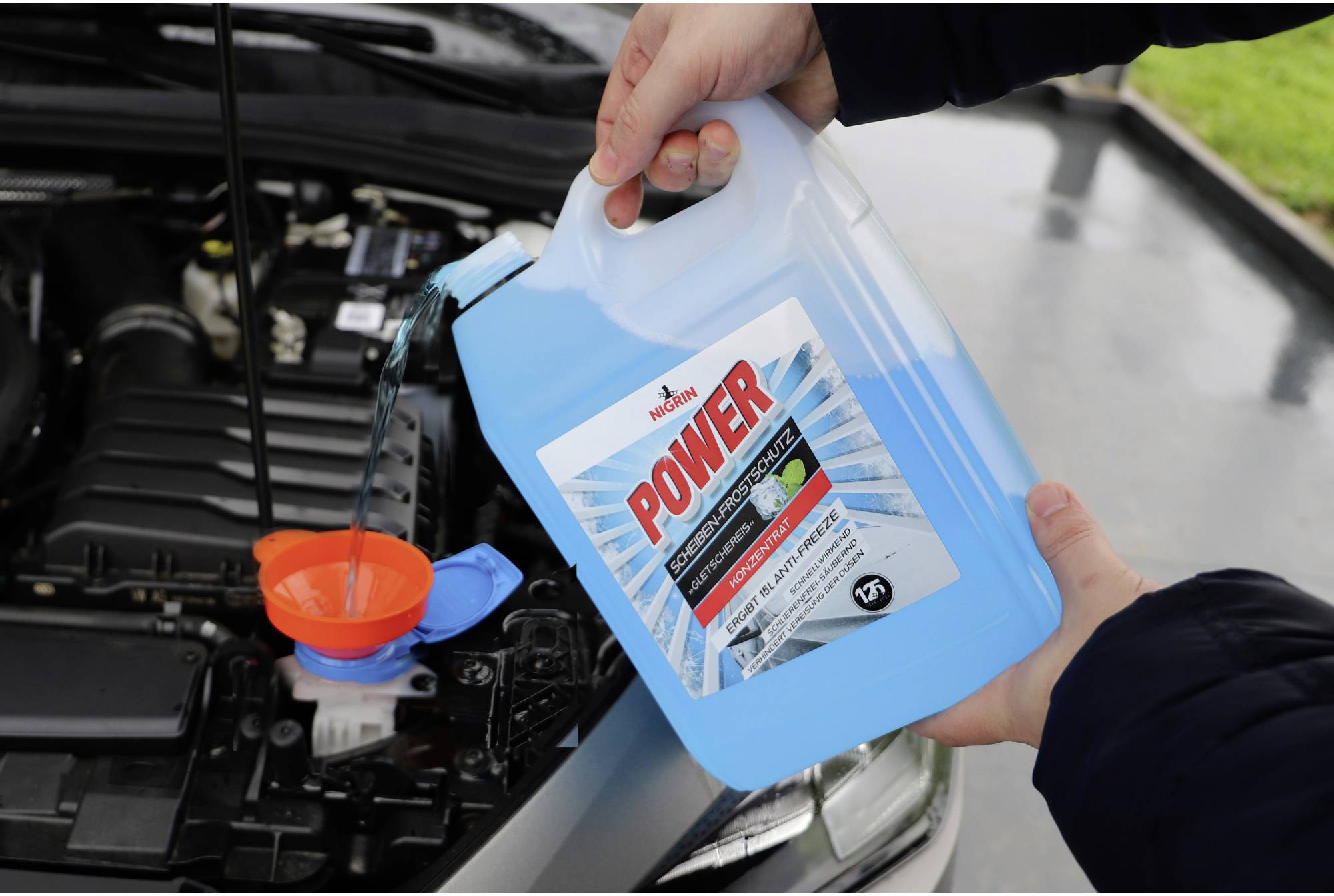A person is pouring blue coolant from a container into a car's engine to ensure engine cooling.