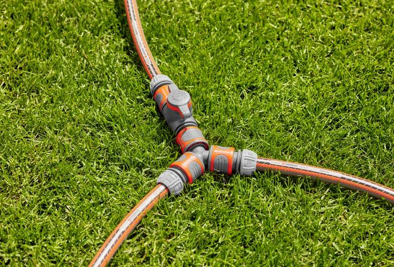 A three-way hose connector links three garden hoses, creating a Y shape on green grass, facilitating multiple water flows.