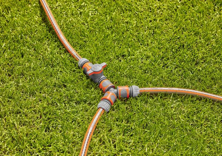 Lawn with a Y-shaped garden hose connector, linking three orange hoses on green grass.