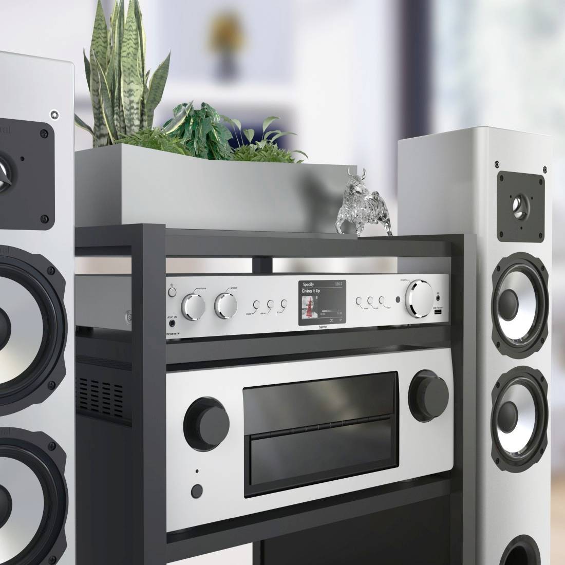 Stereo system with two speakers, an amplifier, and a plant arrangement on a shelf. Living room in the background.