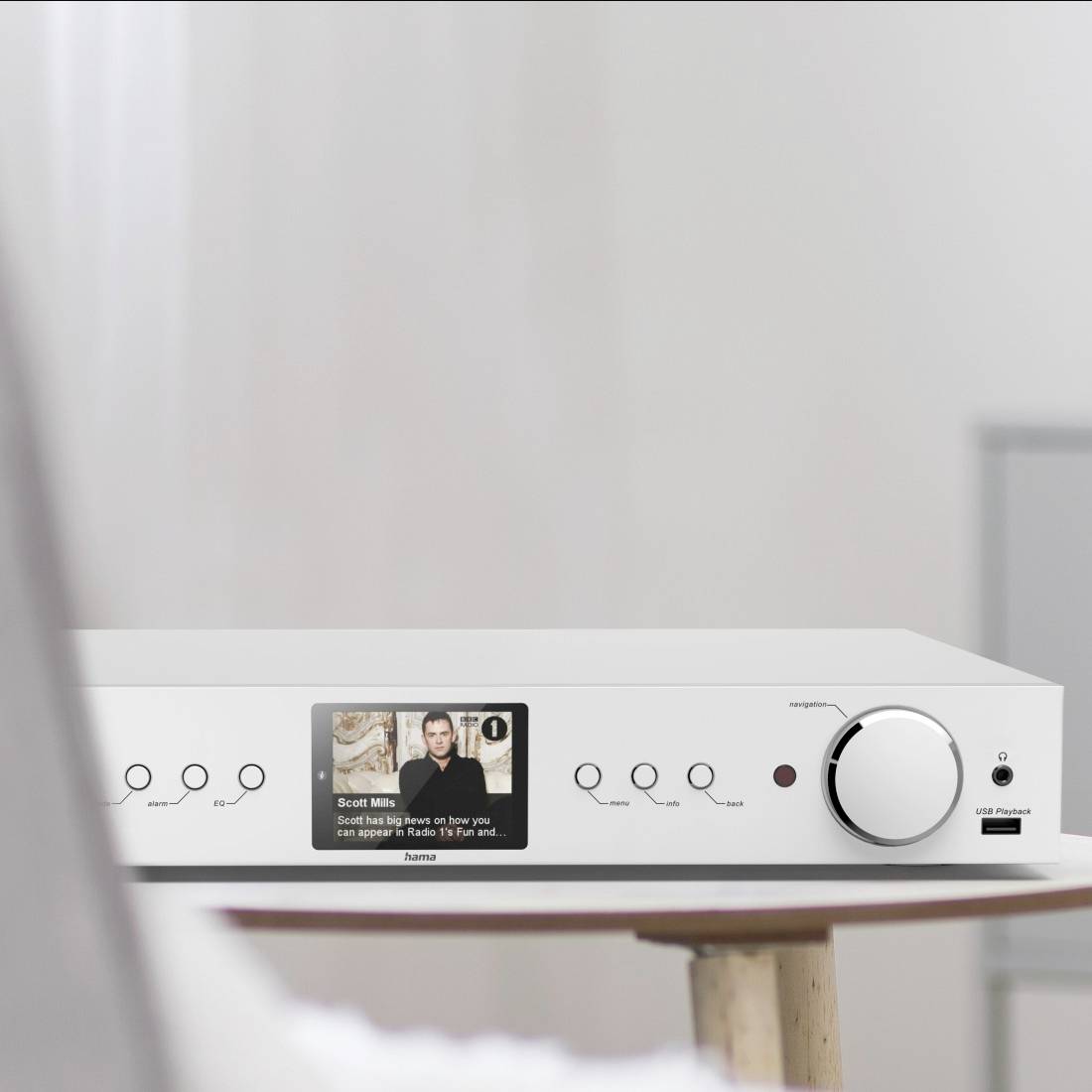 A modern audio amplifier sitting on a table, with a large volume control dial and a display showing a music track.