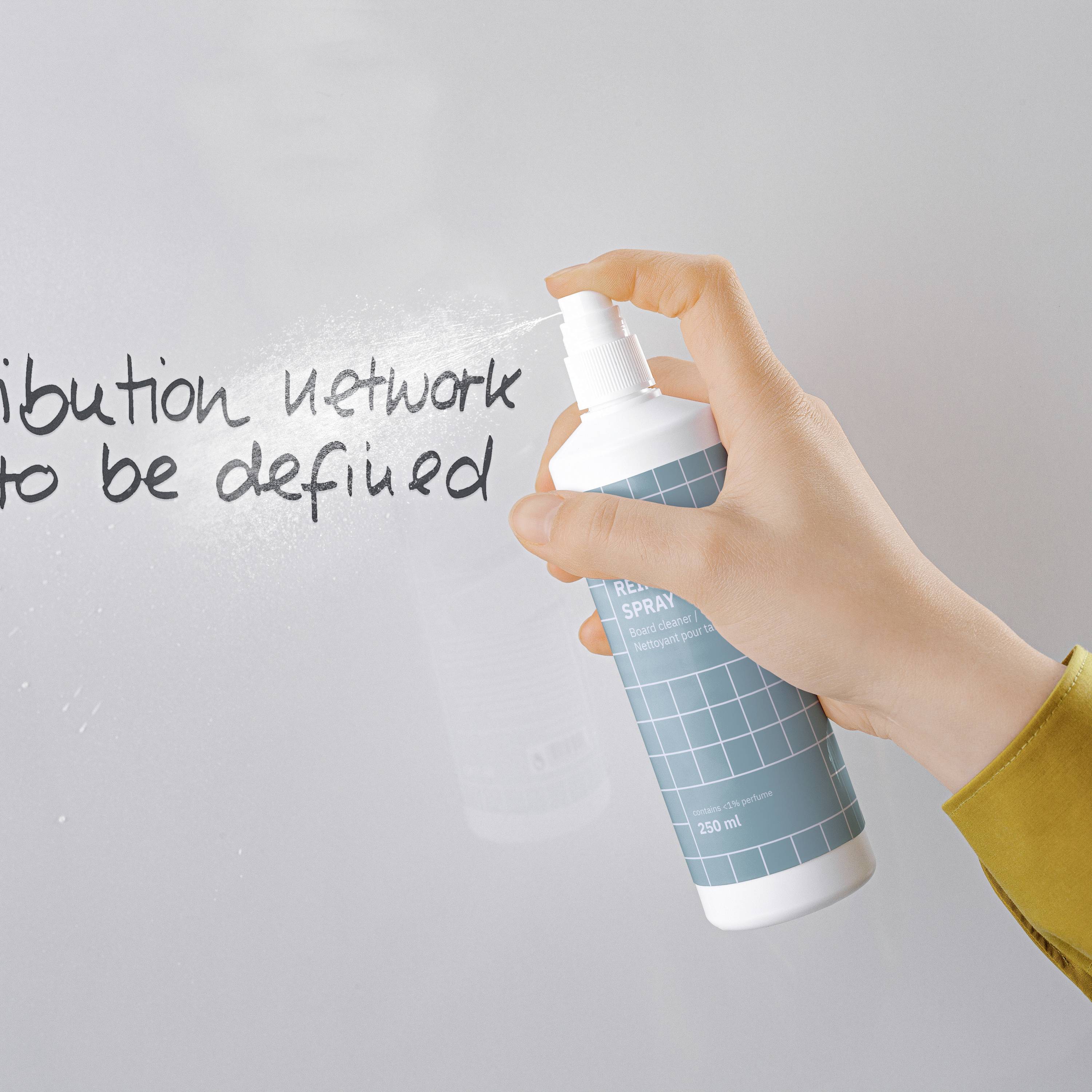 A hand is holding a bottle of spray with 'REDACTED SPRAY' written on it. Blurred text is visible on a board in the background.