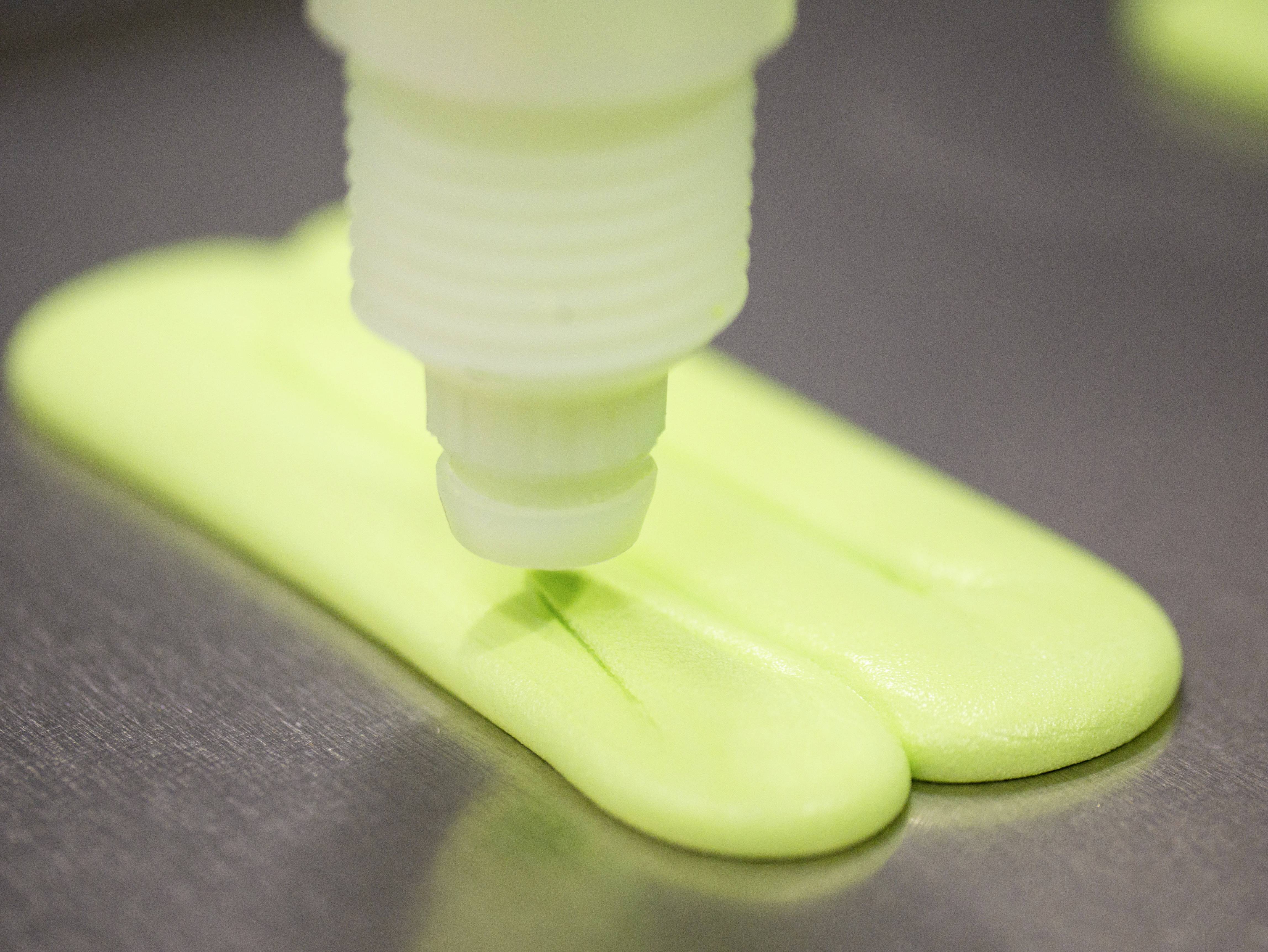 A device is spreading green matter onto a flat surface. The scene depicts an industrial production process.