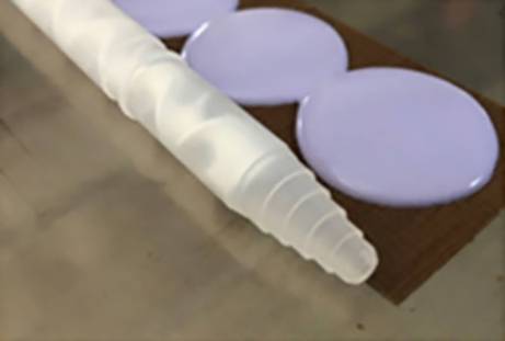 White, milky cylindrical structure beside three round, lilac spots on a brown surface.