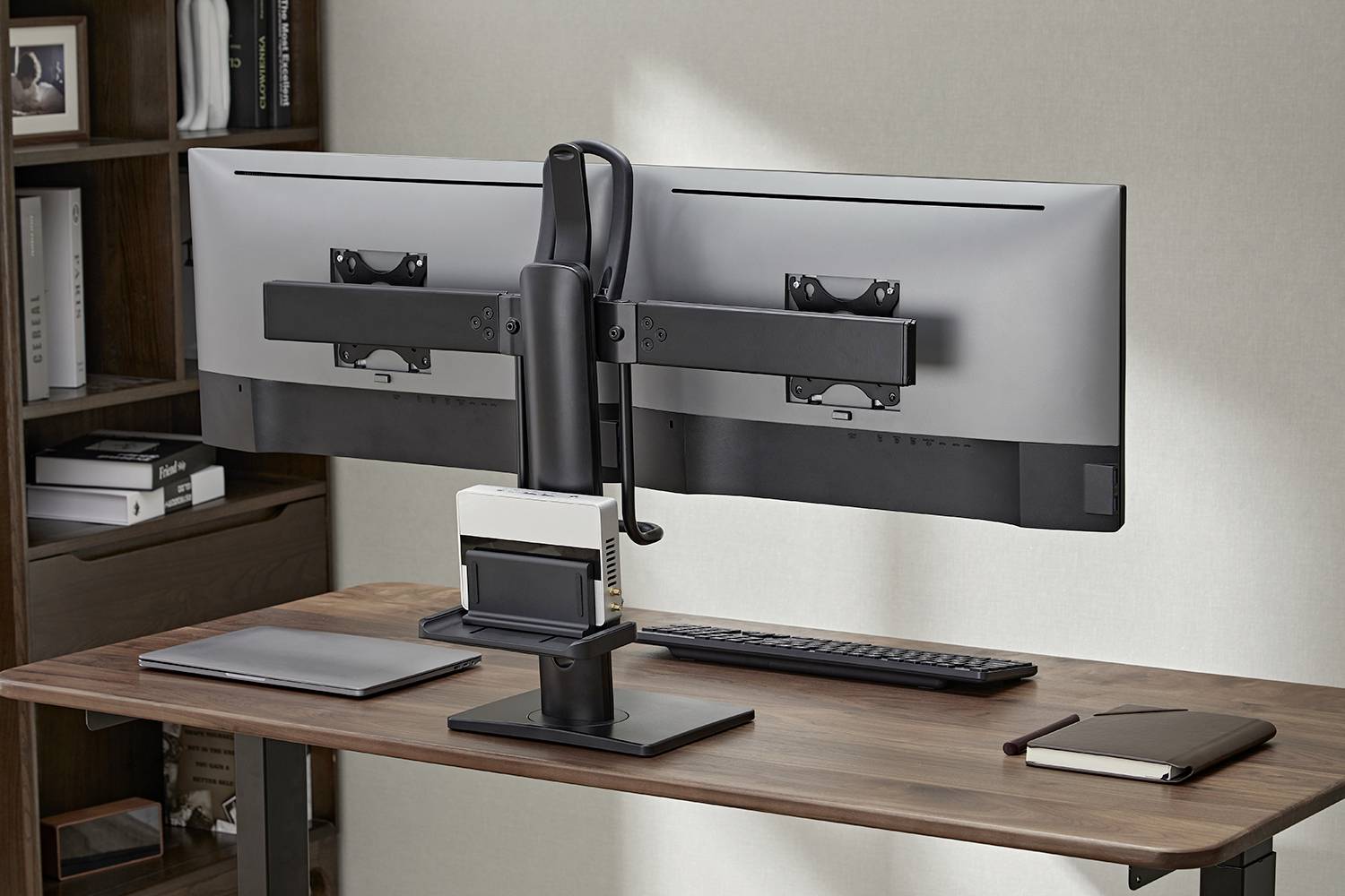Double computer monitors are mounted side by side on a desk, with a keyboard and a notebook underneath.