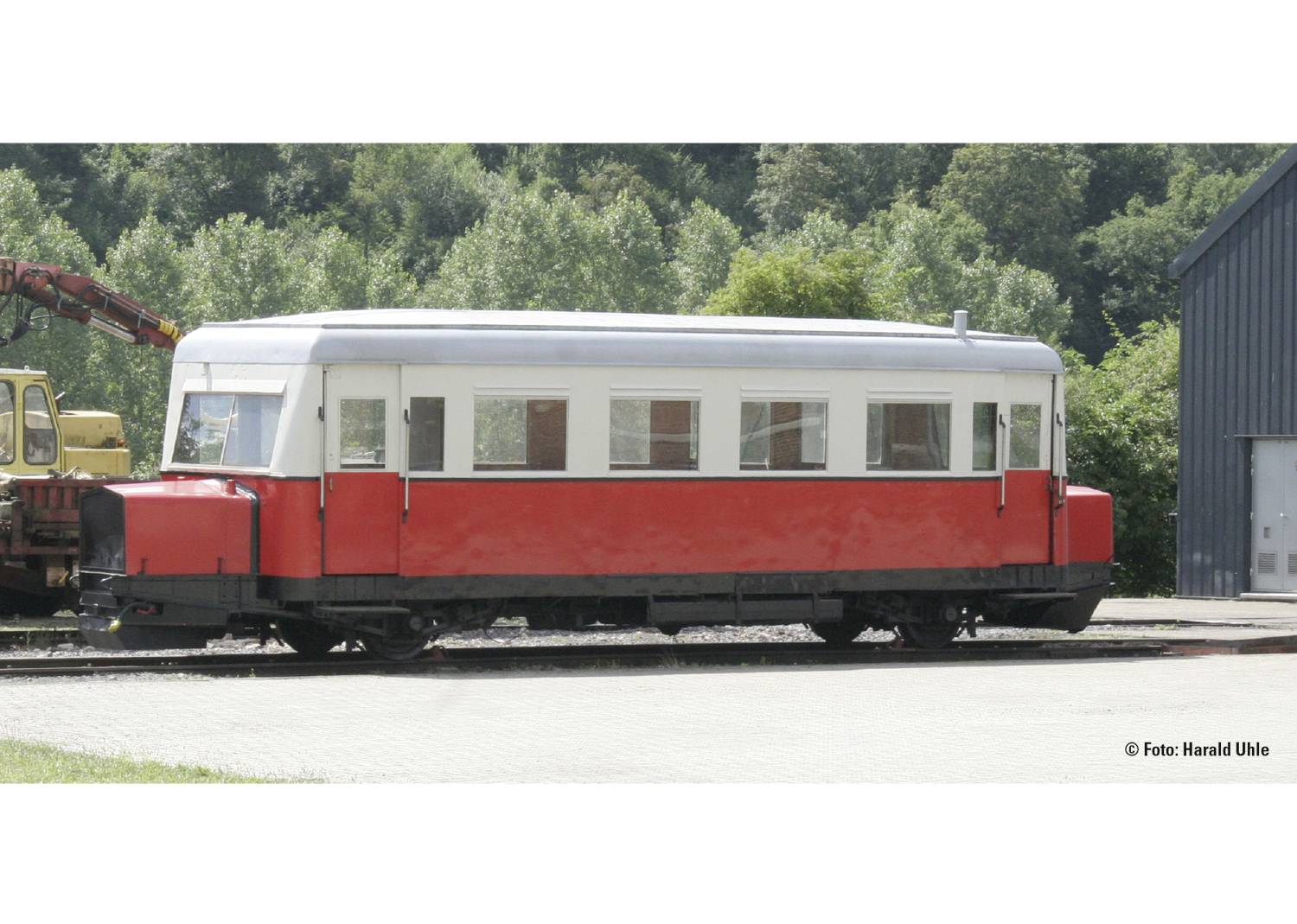 A historic red rail bus stands on a track in front of a wooded background.