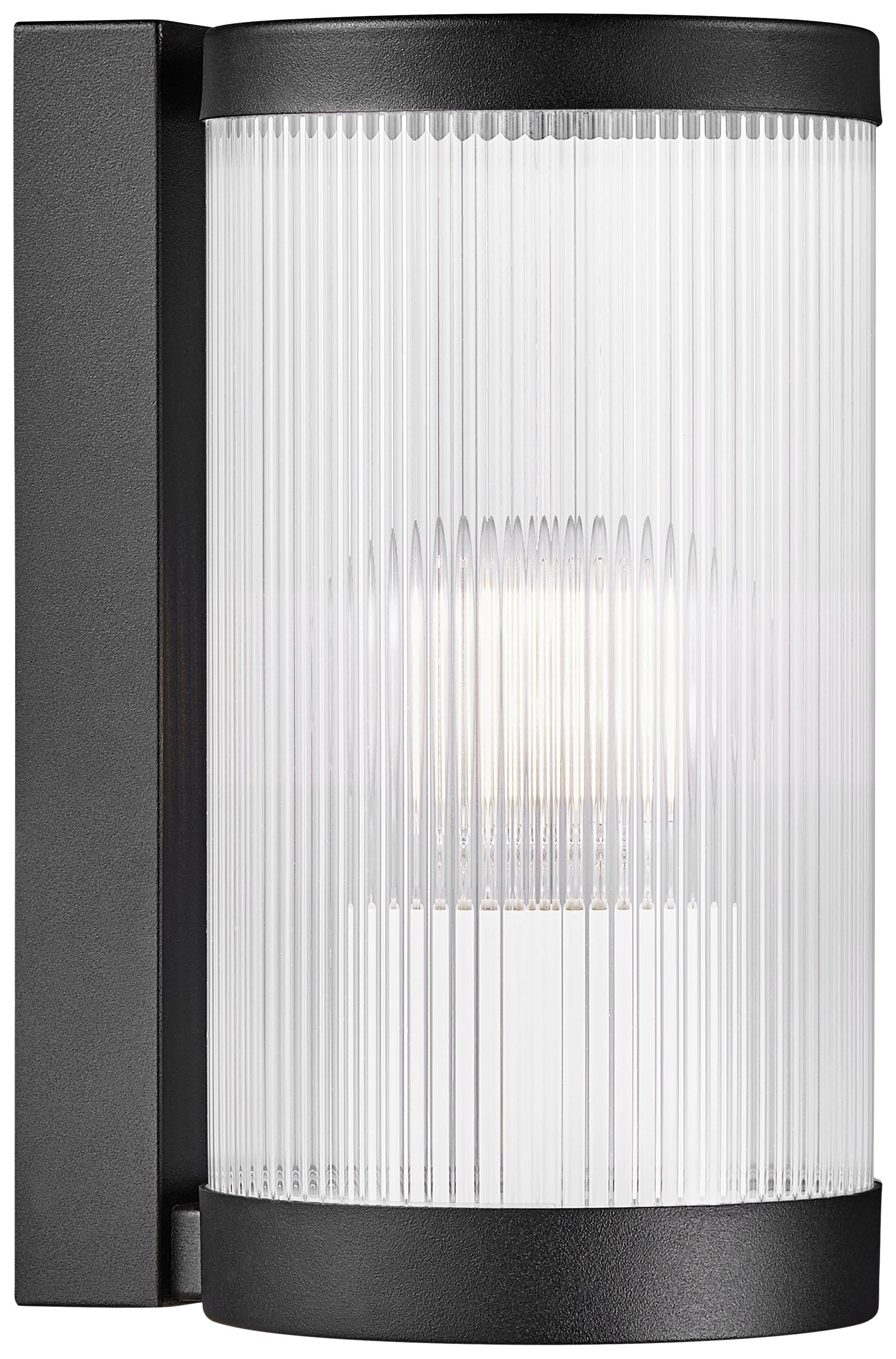 A modern exterior wall light with transparent, ribbed glass and a black housing glows with a warm light.