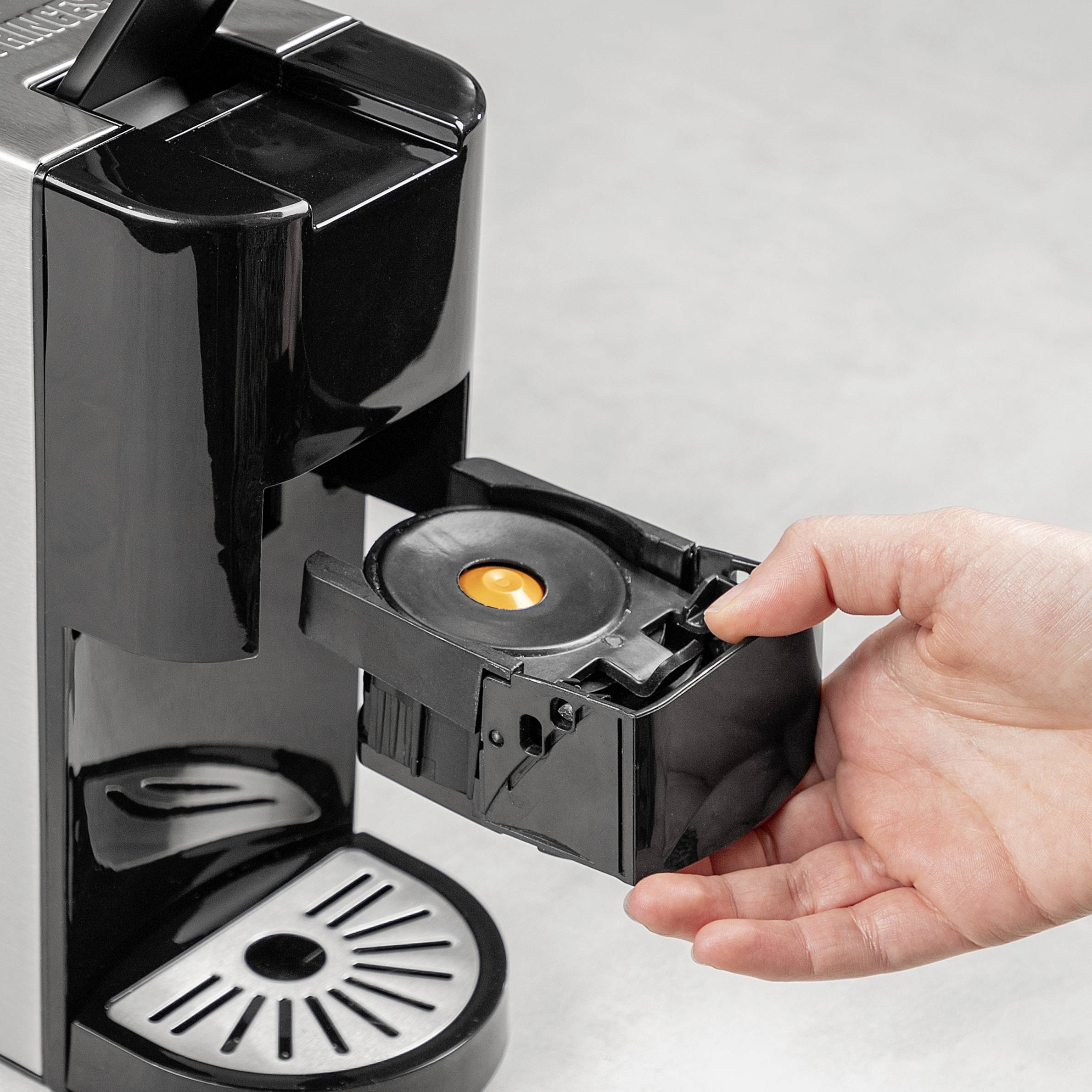 A hand removes a coffee capsule holder from a black coffee machine on a grey surface.