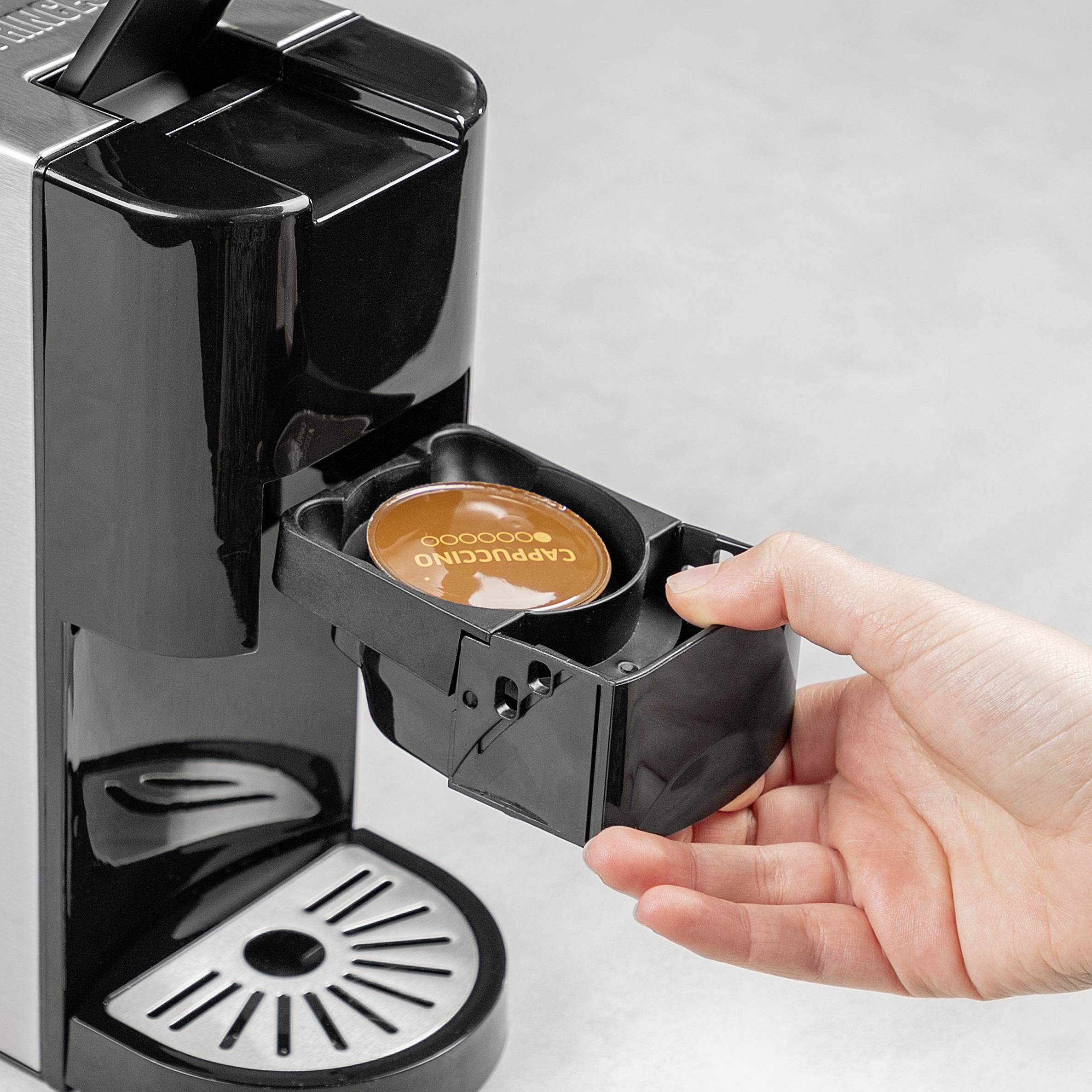 A hand places a coffee capsule into a capsule machine. The machine and capsule are in focus, ready for preparation.