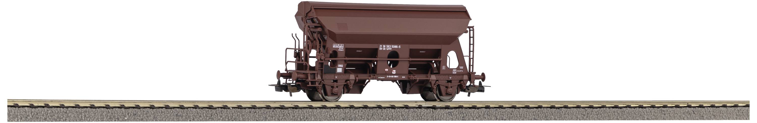 A brown goods wagon is standing on railway tracks. The wagon has a trapezoidal cargo chamber and is positioned sideways on a flat section of track.