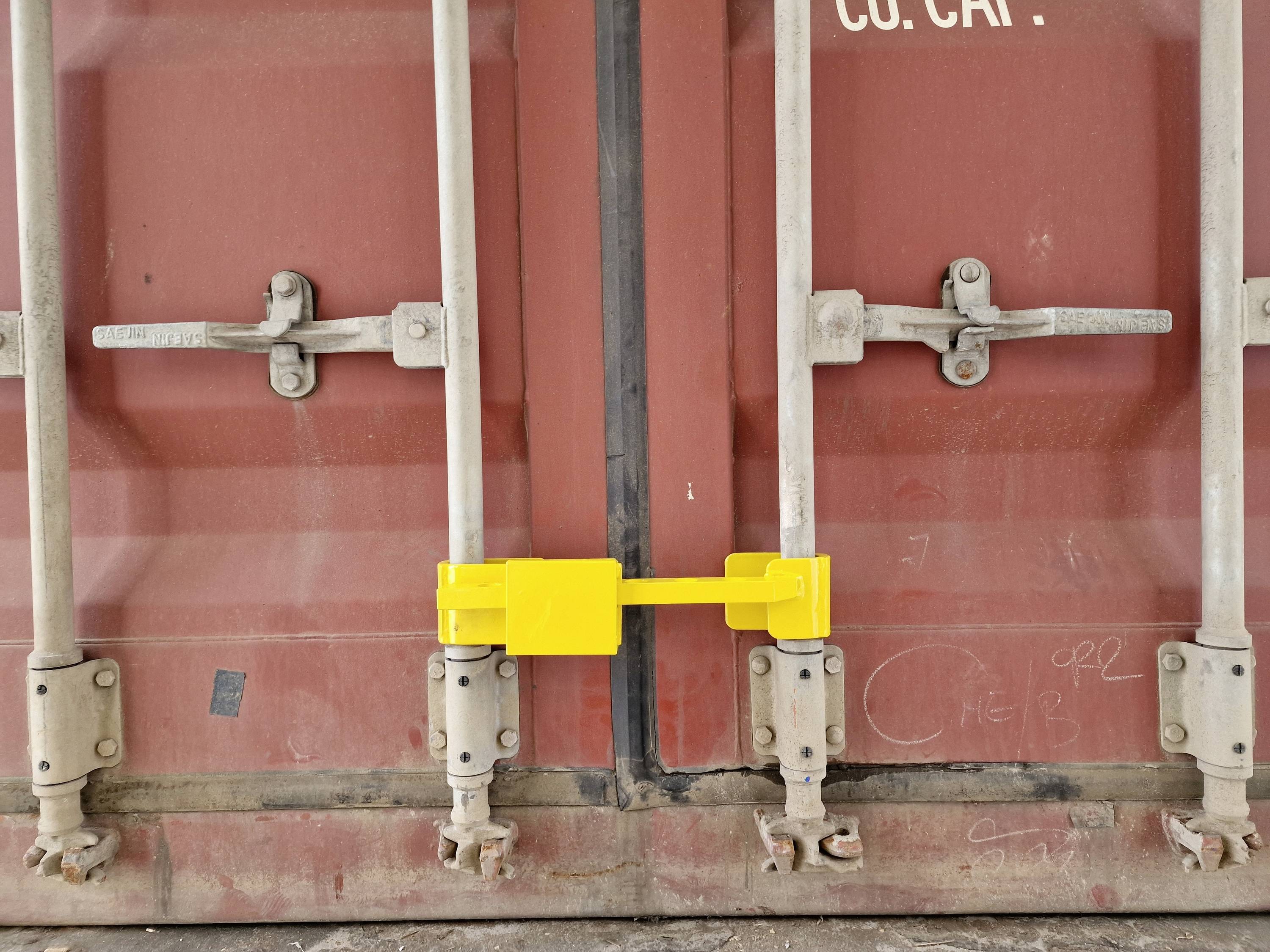 A red shipping container with a yellow lock on its double doors. The surroundings appear industrial.