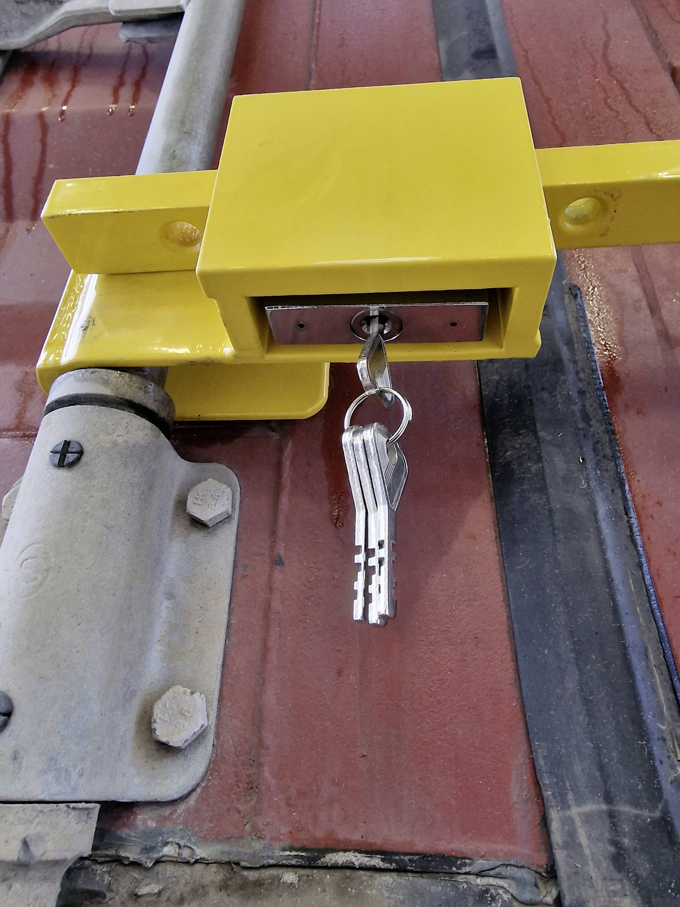 A yellow padlock on a metal gate with keys inserted in the loop, mounted on a red background.
