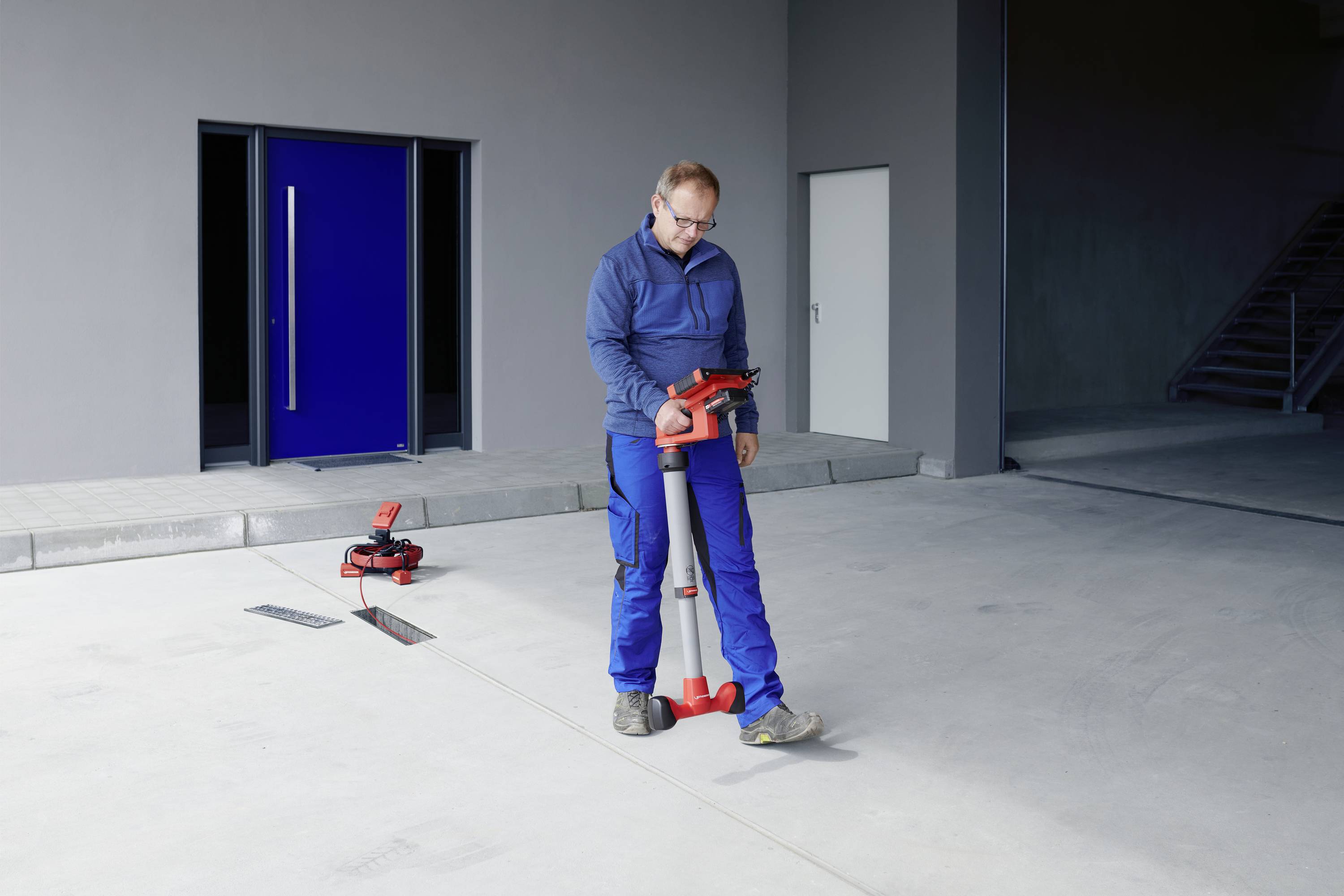 A person in workwear is operating a surveying instrument in an empty hall. Another instrument lies in the background.
