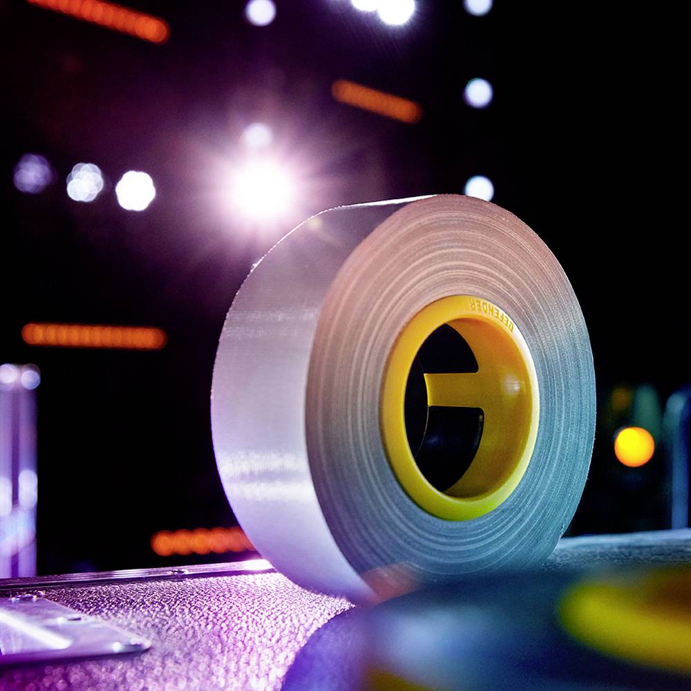 A large, silver gaffer tape stands on a stage illuminated by colourful lights. It appears to be used for stage work.