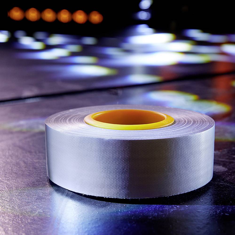 A large roll of silver gaffer tape lies on a shiny surface, surrounded by colourful lights reflecting on the floor.
