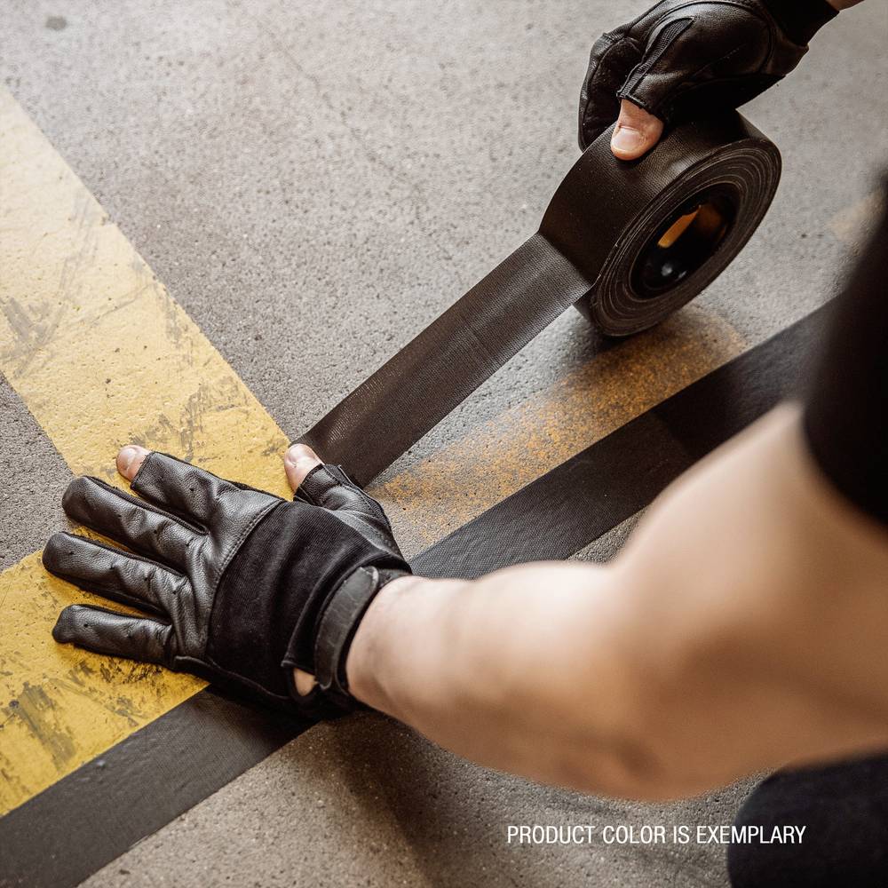 A person wearing black gloves is sticking black adhesive tape along a yellow line on the floor.