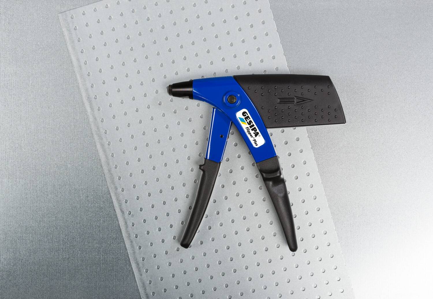 A blue pair of pliers lies on a silver, perforated metal sheet.