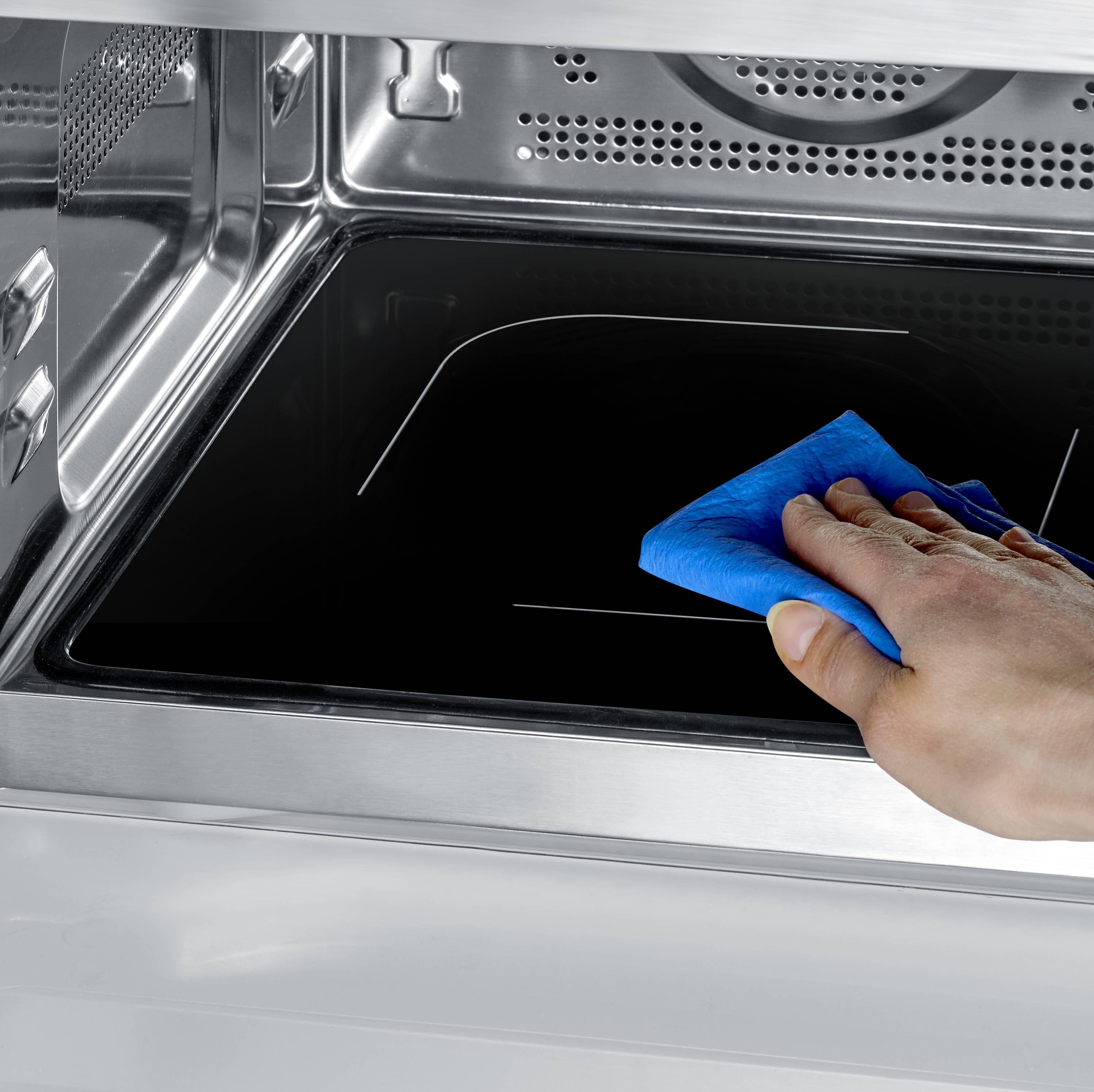 A hand is wiping the inside of a clean microwave oven with a blue cloth.