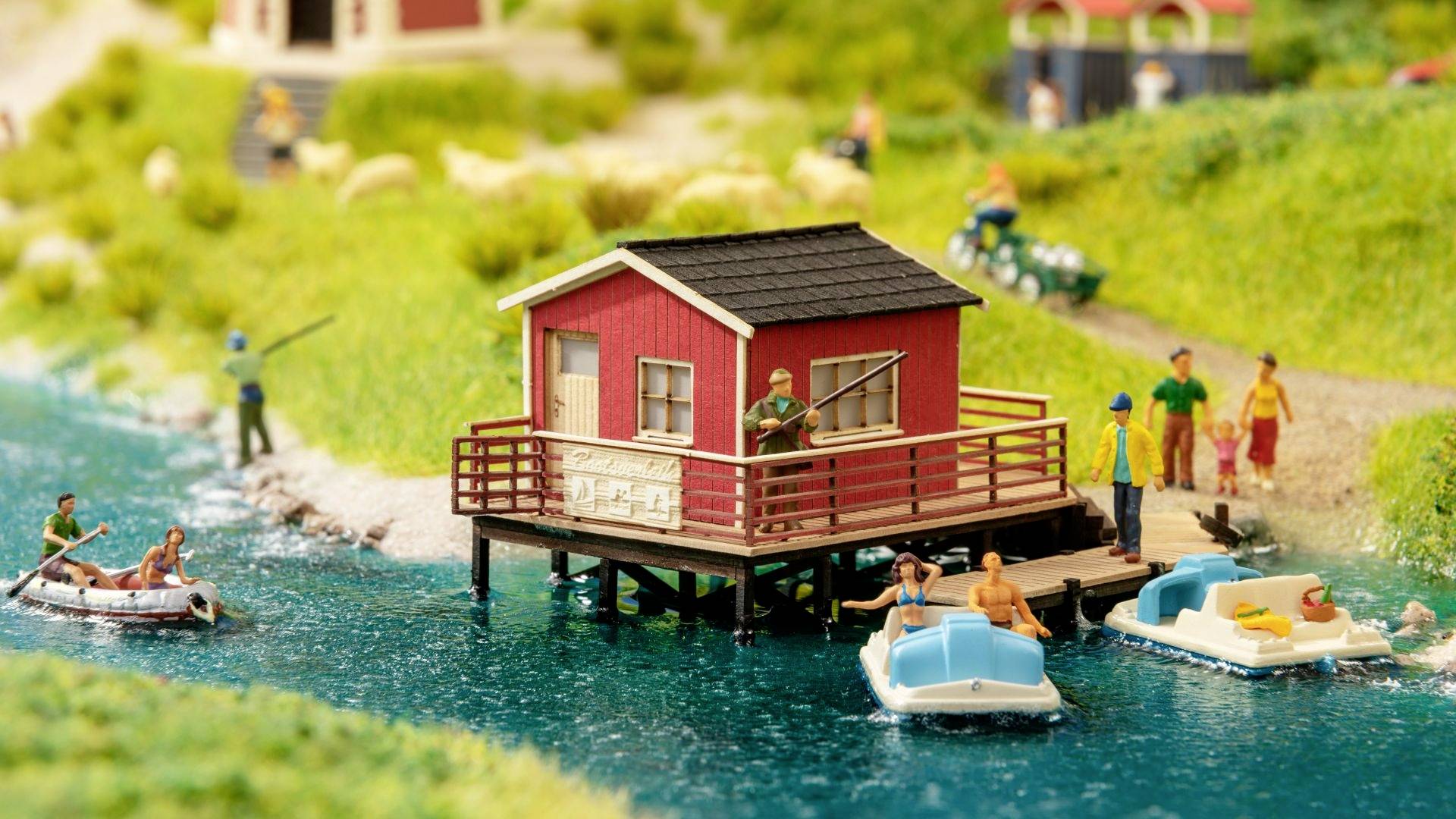 A model of an idyllic waterside landscape with a red house on a jetty, boats in the water, and miniature figures fishing and walking.