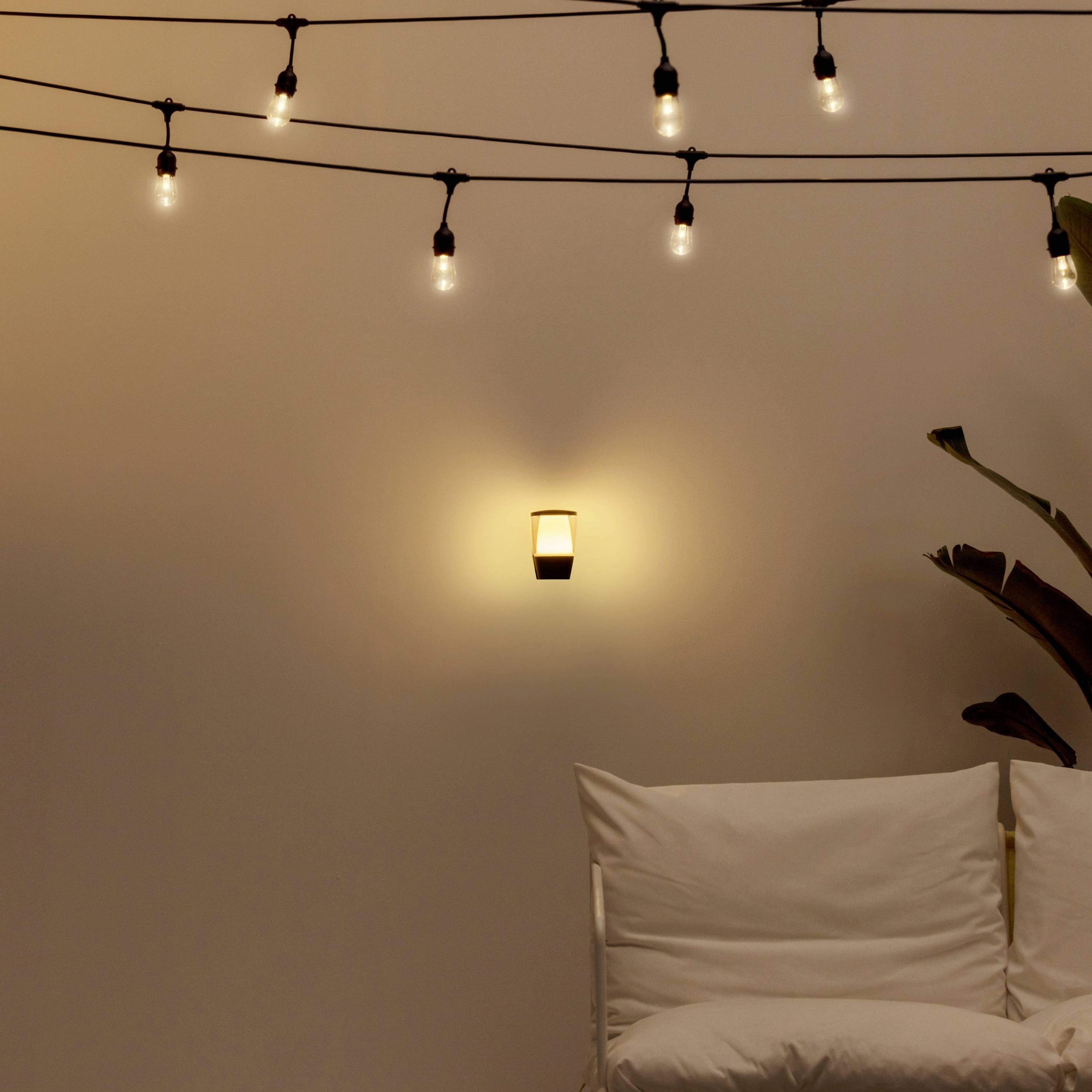 Fairy lights on the wall, a glowing wall lamp, with a white cushion placed on a chair beneath. A relaxed, cosy atmosphere.
