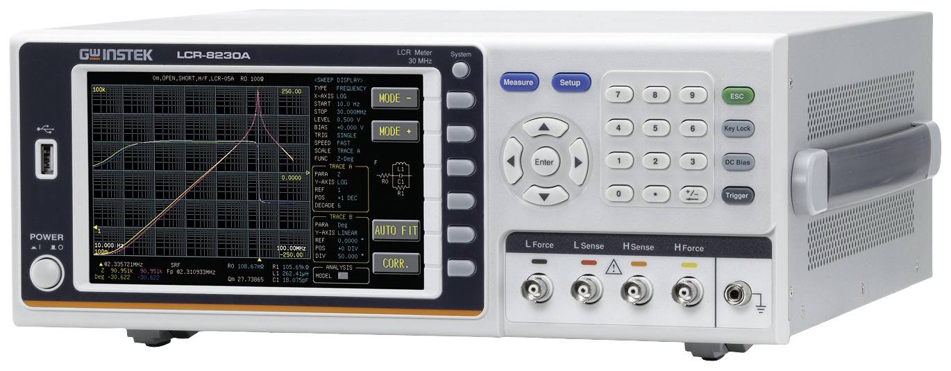 An electronic test device with a digital display shows graphical measurement data. Control buttons and connectors are present.