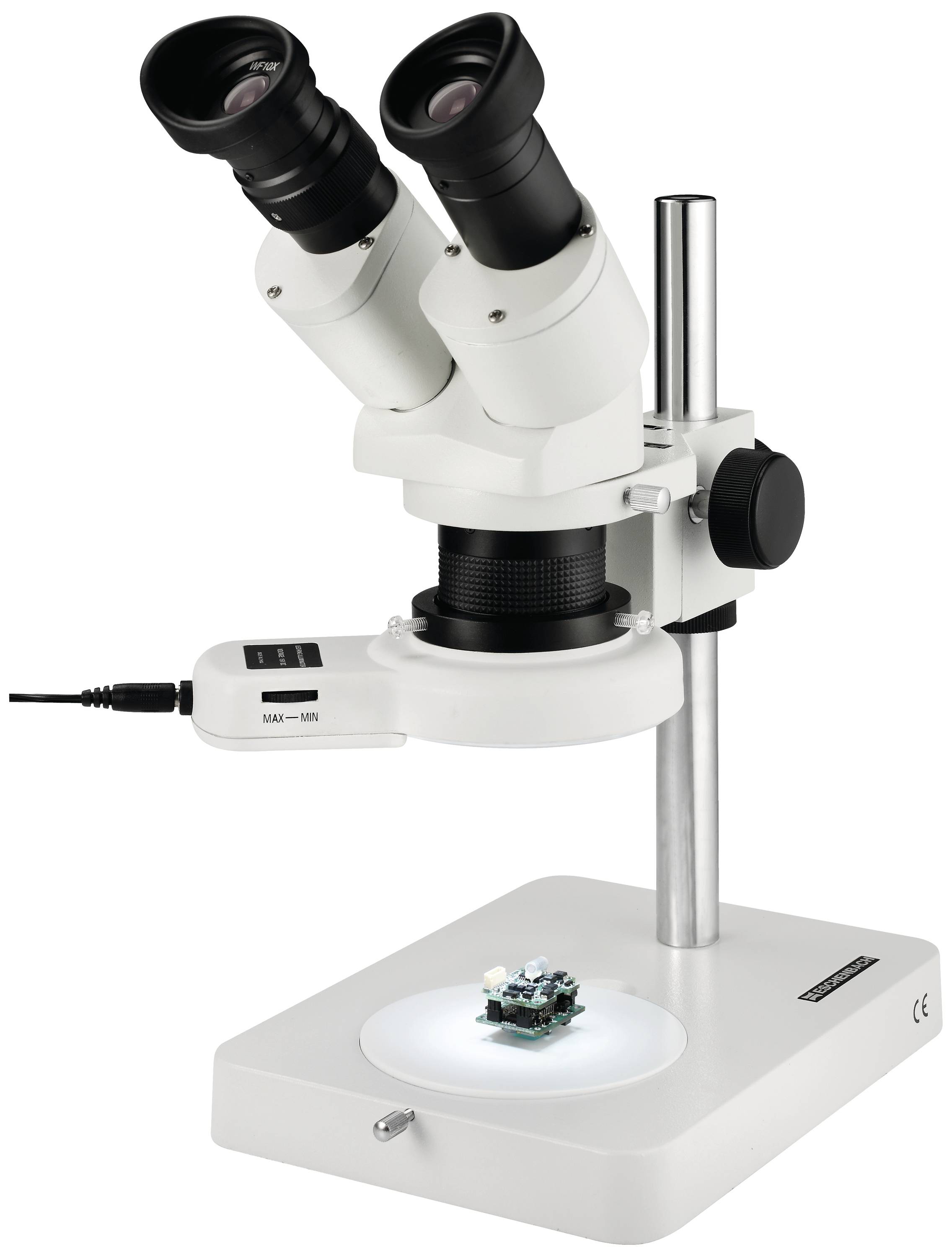 A white stereo microscope with two eyepieces stands on a table. Beneath it, a small electronic circuit lies on the illuminated base.