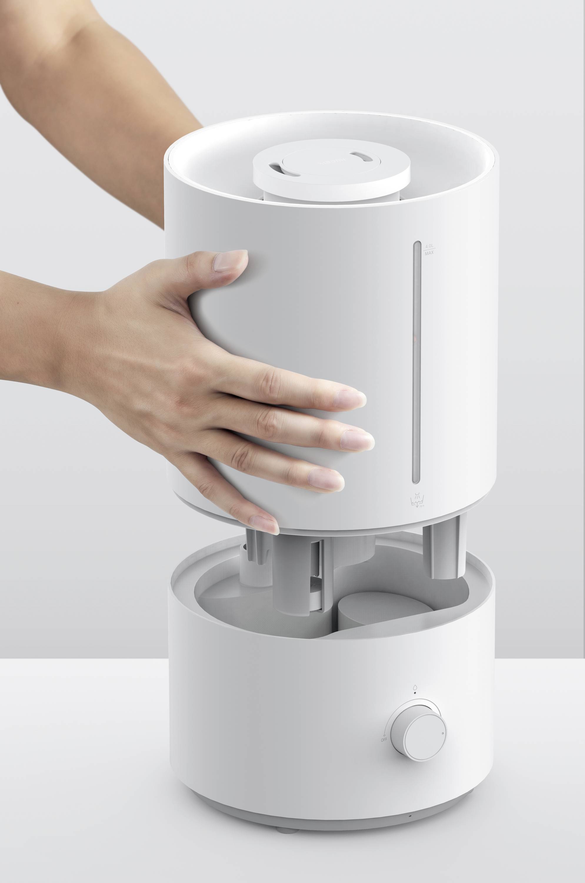 A person opens a white air humidifier by removing the top section. The air humidifier has a simple, modern design.