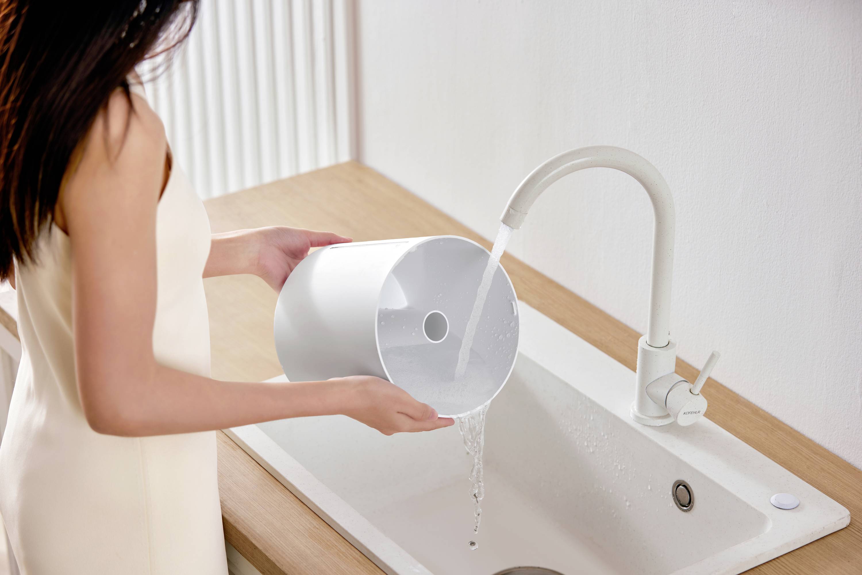 A person is filling a white jug with water from the tap at a sink.