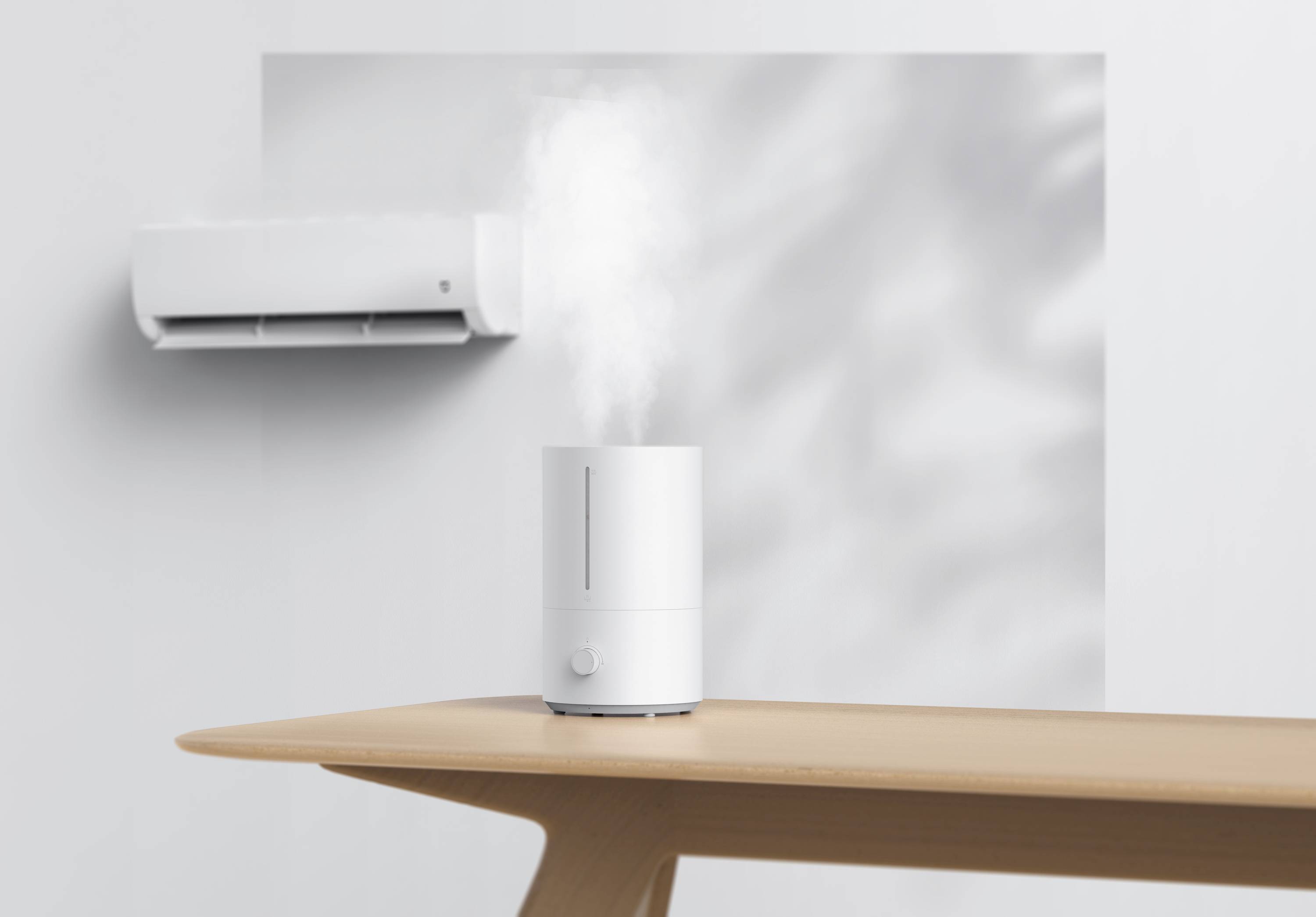 A humidifier is releasing steam on a wooden table. In the background, an air conditioning unit can be seen on a white wall.