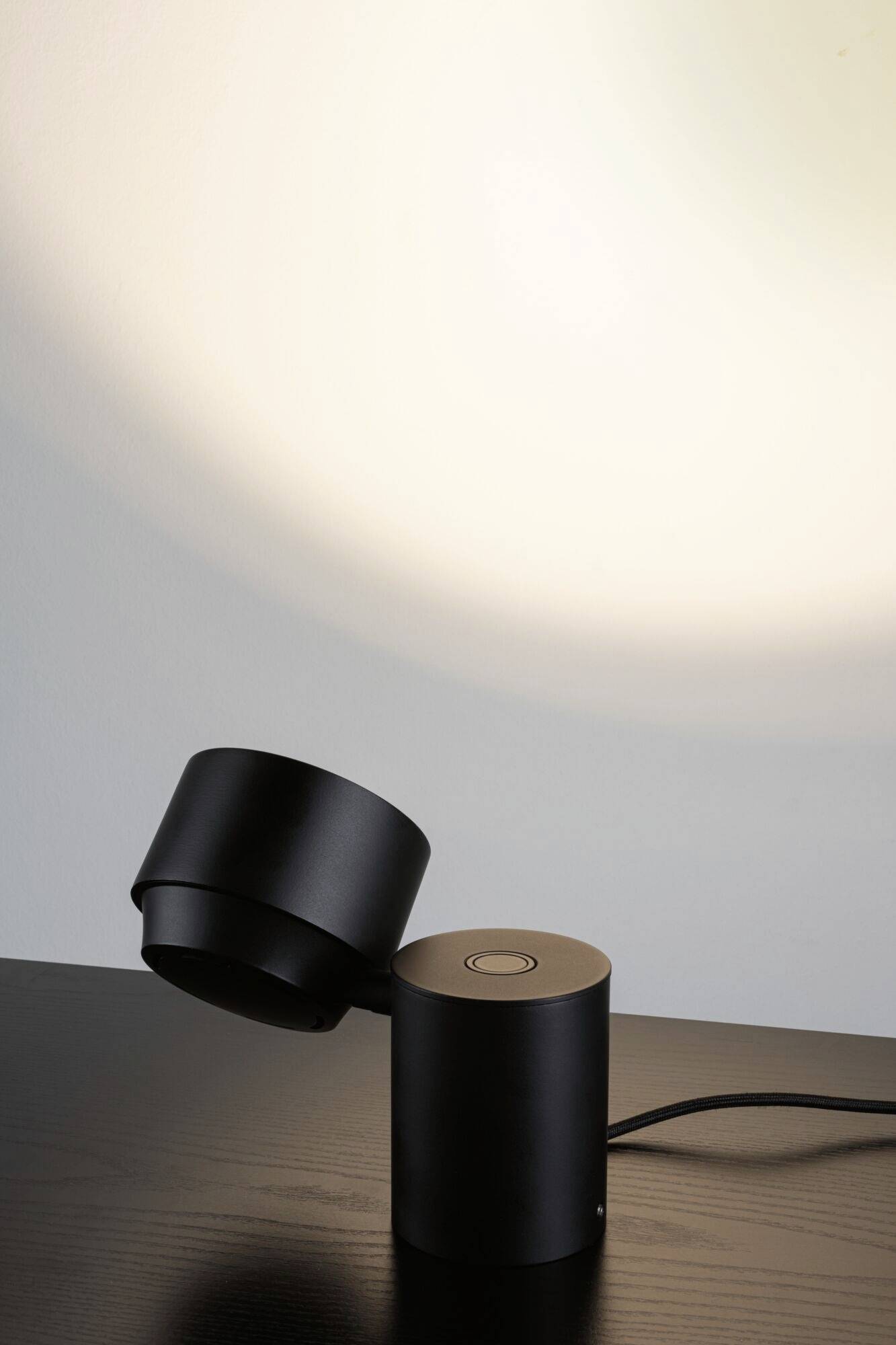 Black table lamp with modern design on dark wooden table, illuminating wall in soft light.<br><br>Note: The translation is already in British English, so no significant changes were needed.