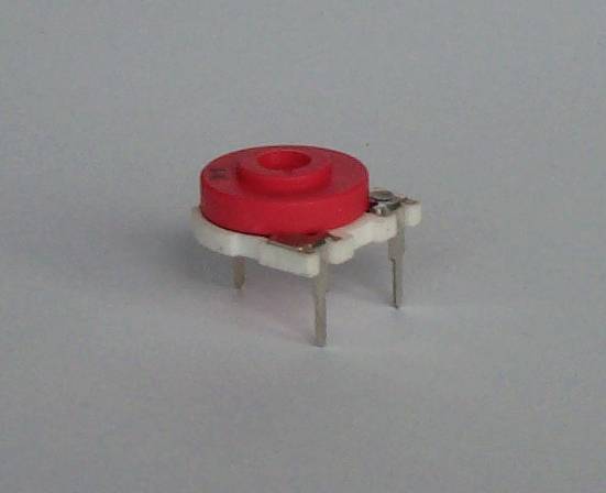 Red, round electronic switch with multiple ports, placed on a white surface.