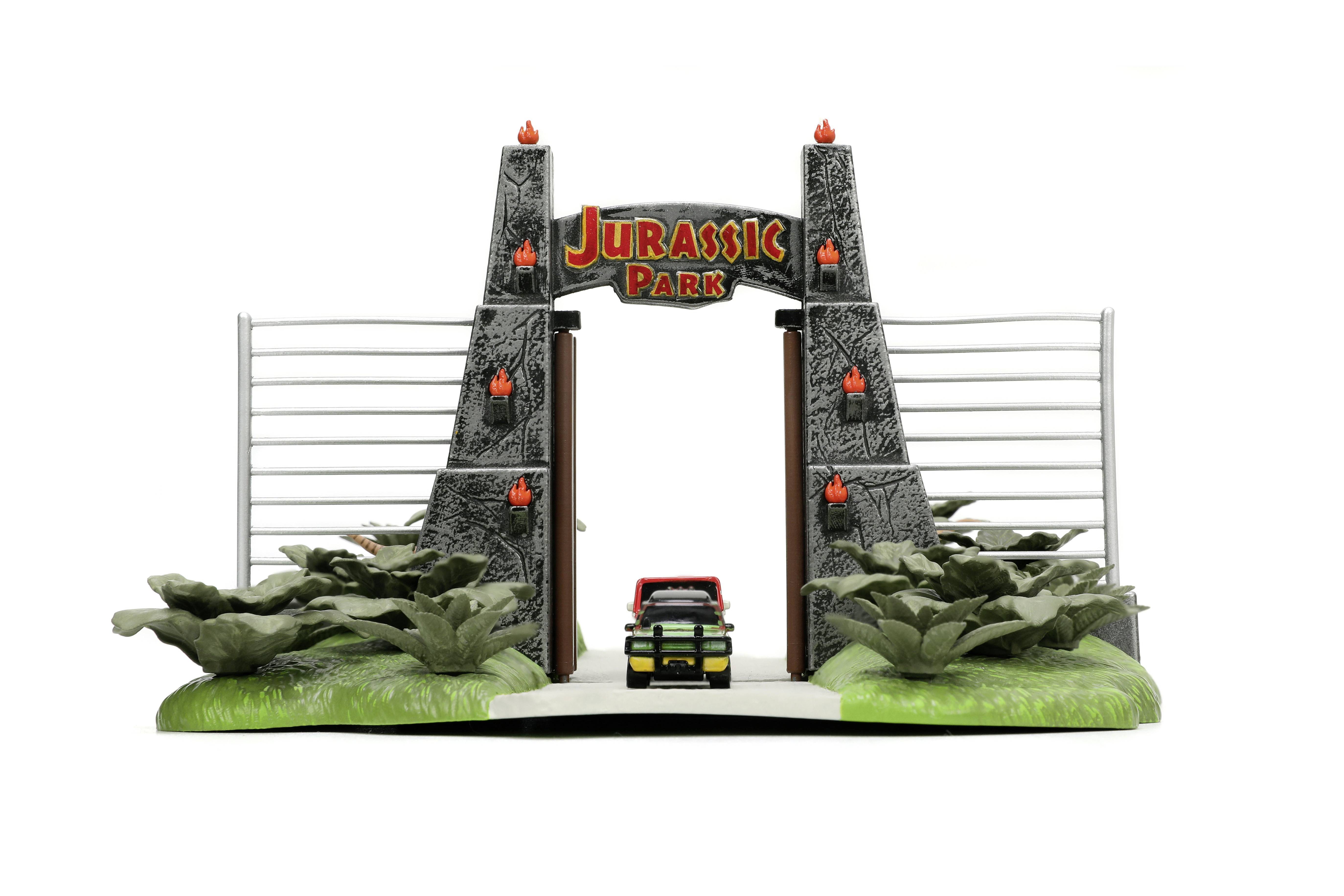 Model of an entrance gate with a 'Jurassic Park' sign, red Jeep, and artificial plants, reminiscent of a film scene.