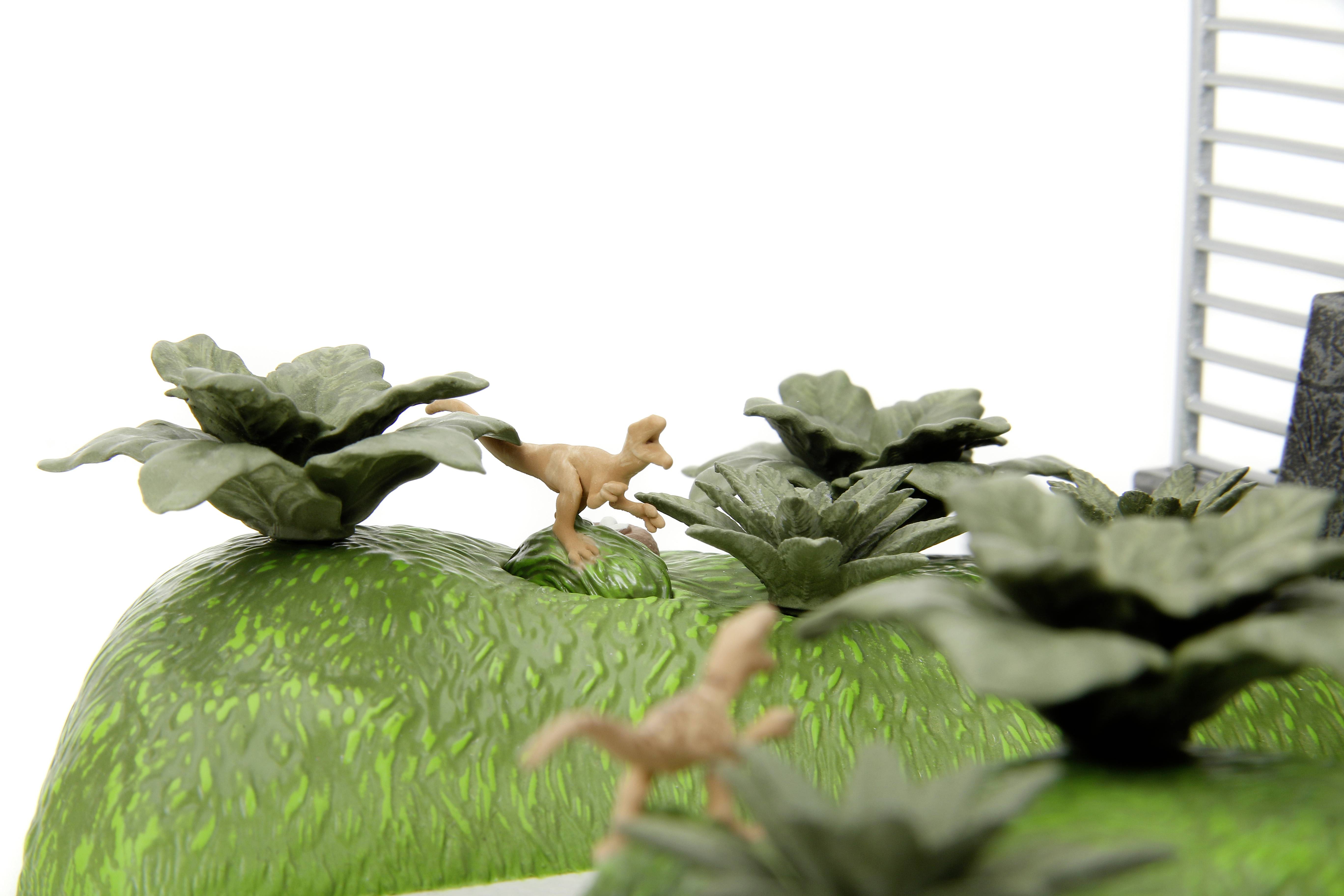 A small plastic toy dinosaur stands among green plastic plants on an artificial green hill.