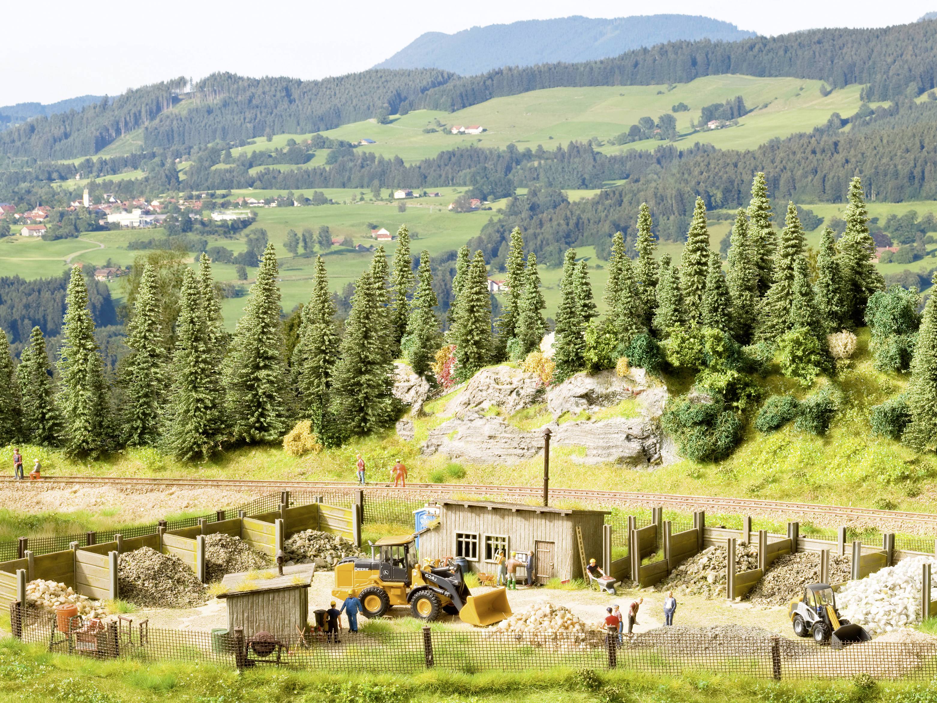 A scenic diorama depicts a construction site with an excavator and workers, surrounded by forests and mountains in the background.