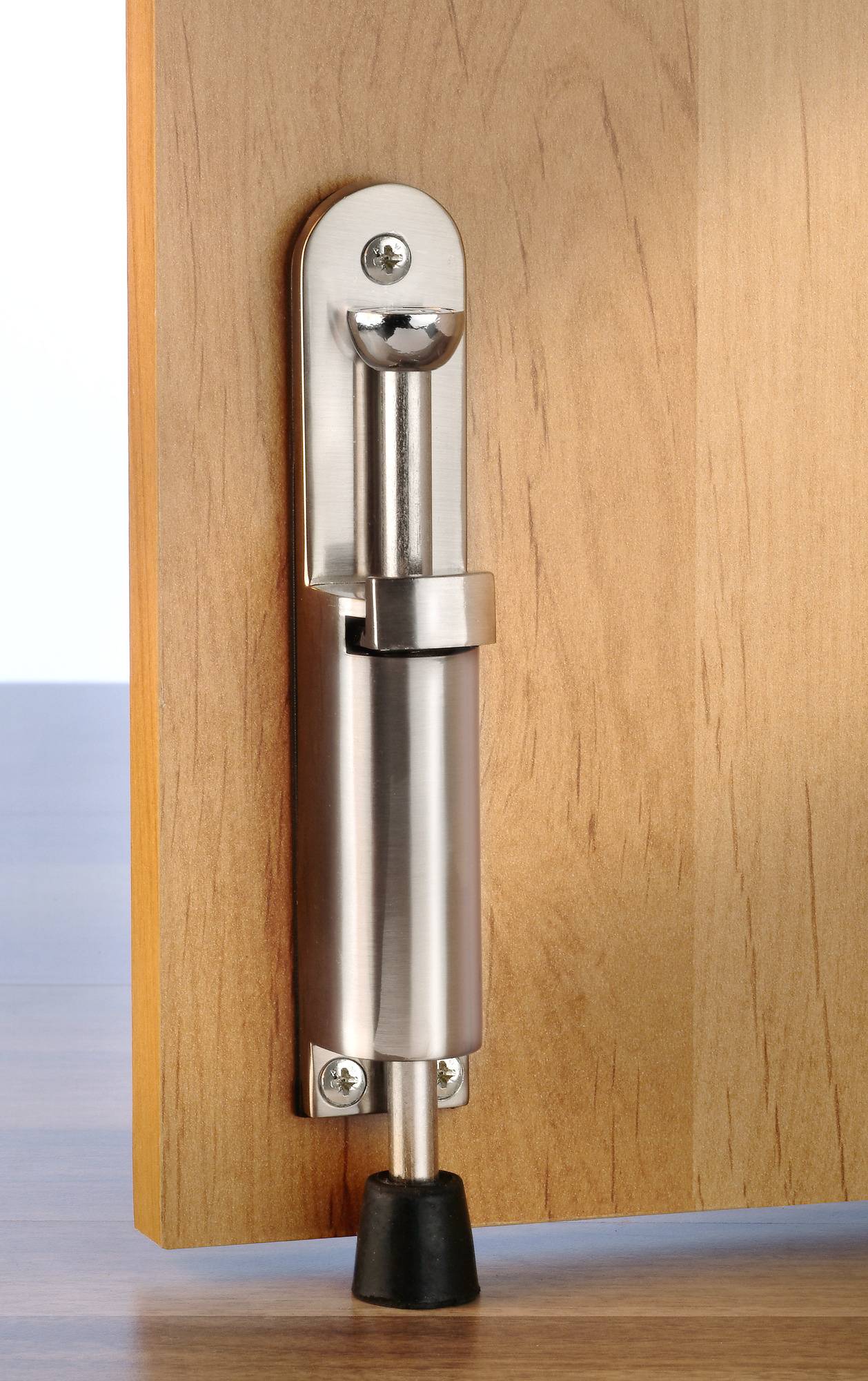 A metal door stop with a rubber cap is attached to a wooden door and touches the floor to hold the door in place.