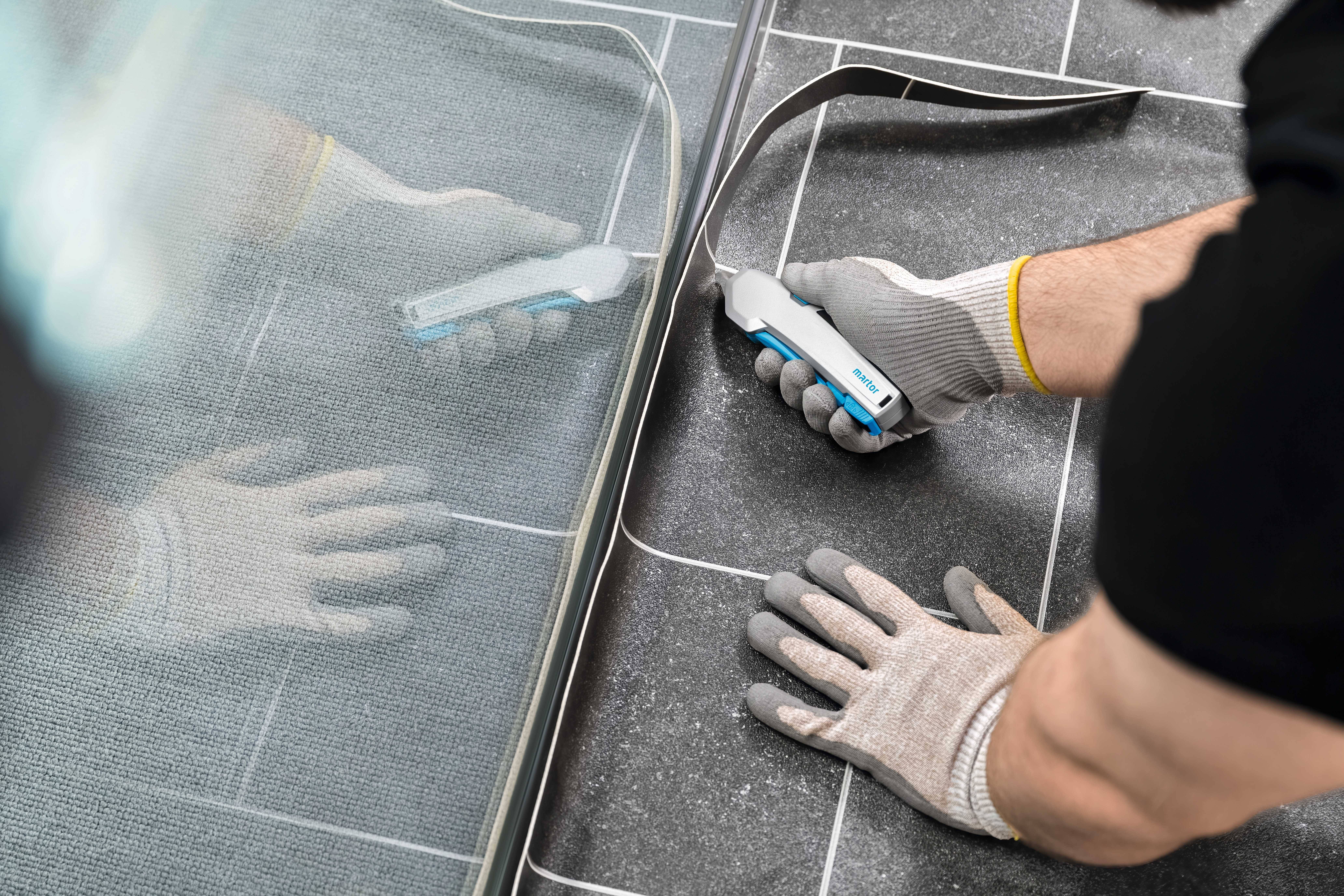 A craftsman applies sealant to the joints between the wall and floor tiles to seal them. He is wearing protective gloves.