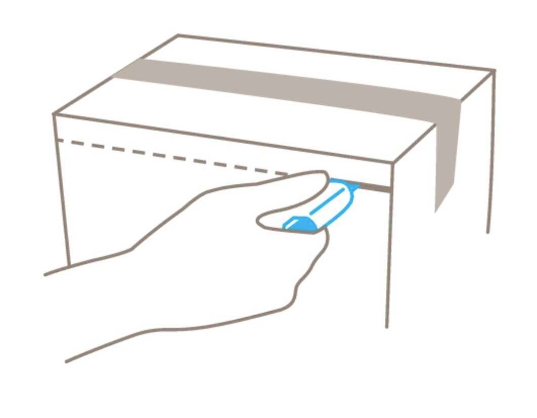 A hand cuts packing tape with a blue Stanley knife on a cardboard box.