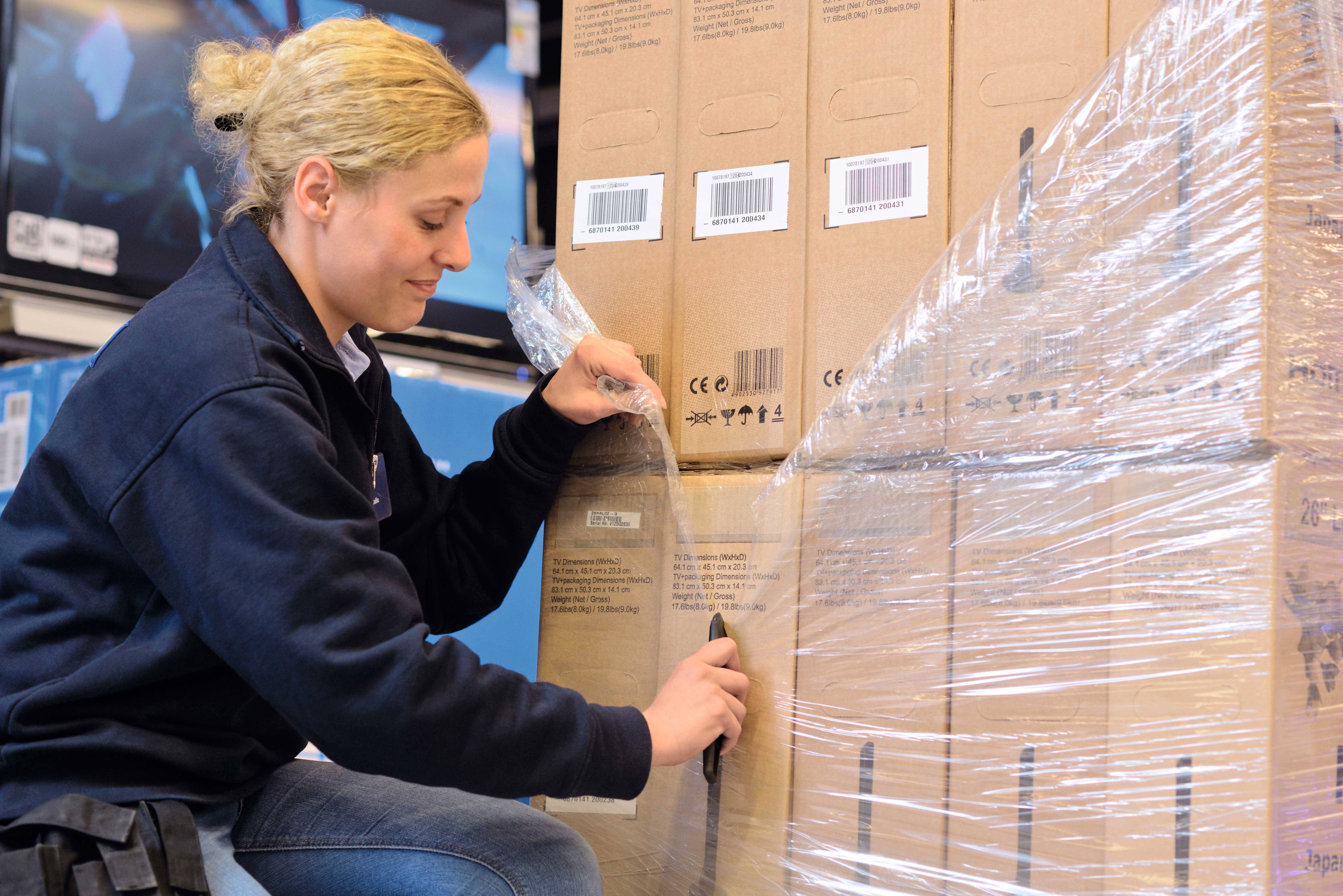 A person opens a pallet of boxes with a knife in a warehouse.