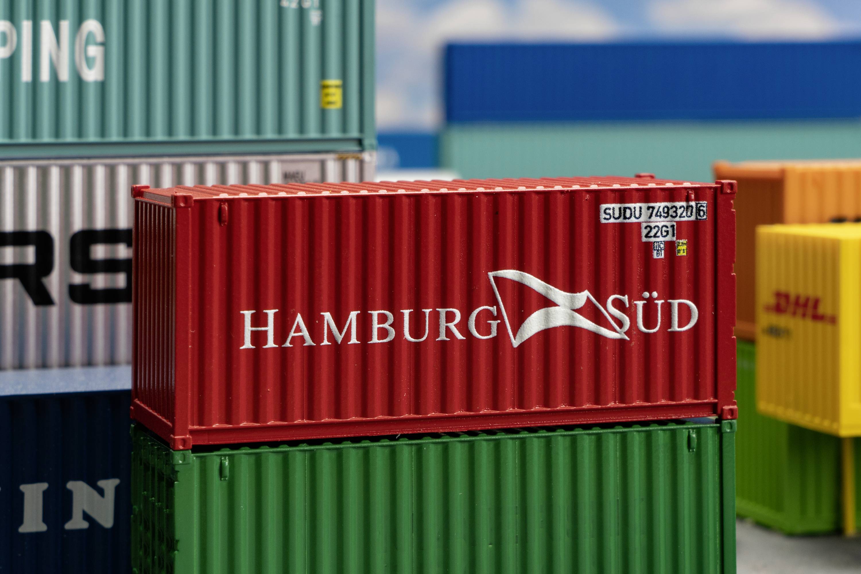 Red freight container with the 'Hamburg Süd' logo stacked amongst other containers in various colours, partially visible.