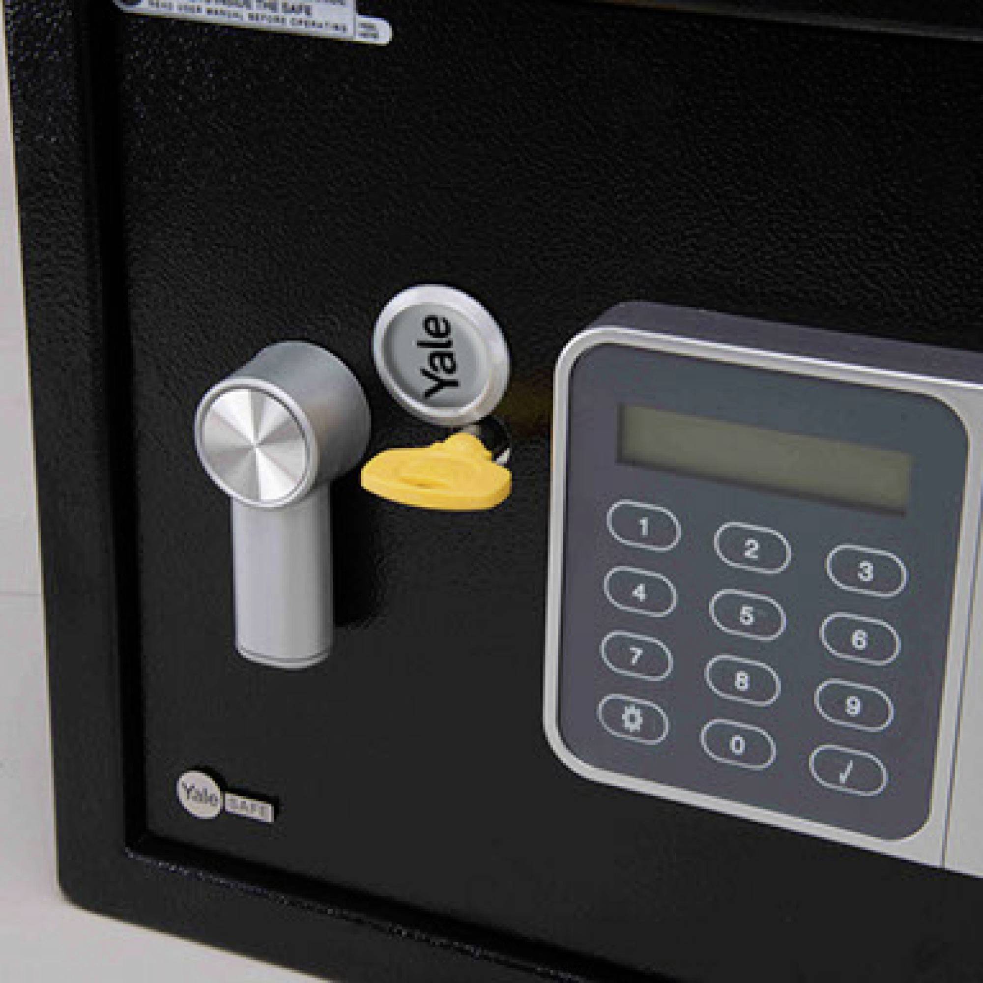 Black-grey Yale safe with digital keypad and rotary handle. Yellow key is inserted in the lock.
